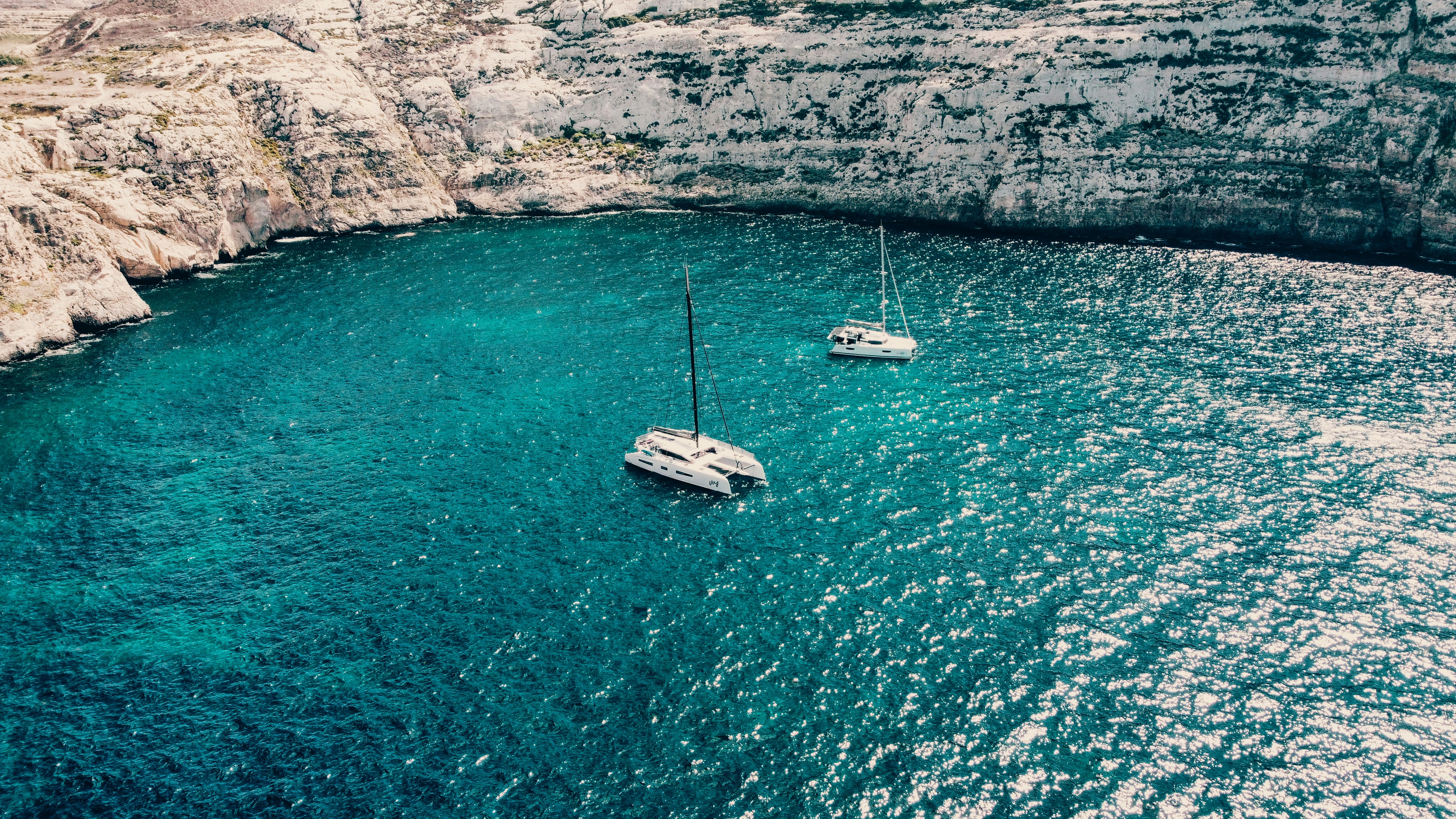 An image of two boats anchored in a gorgeous turquoise harbor surrounded by stone cliffs.