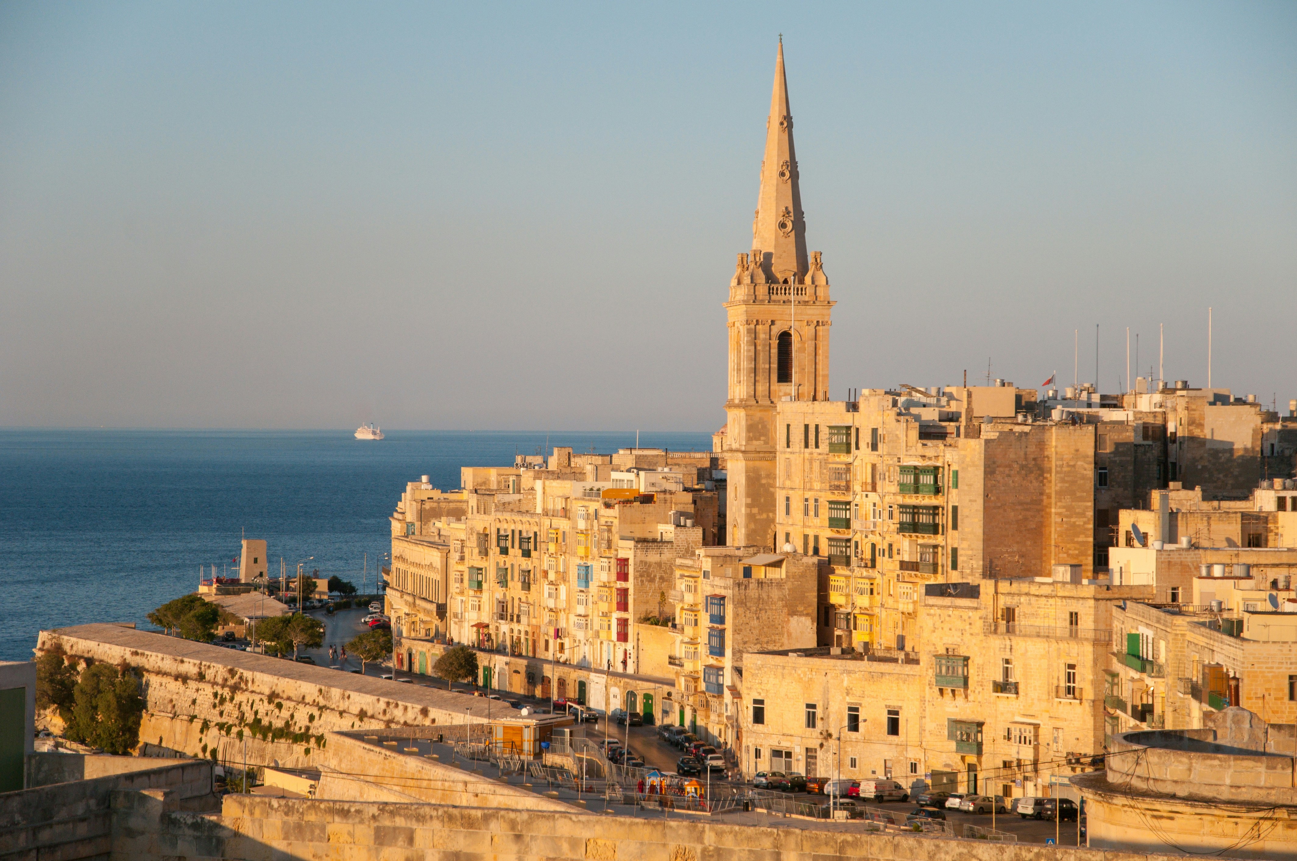 An image of stone buildings and a church tower against a vibrant blue sea and sunset.