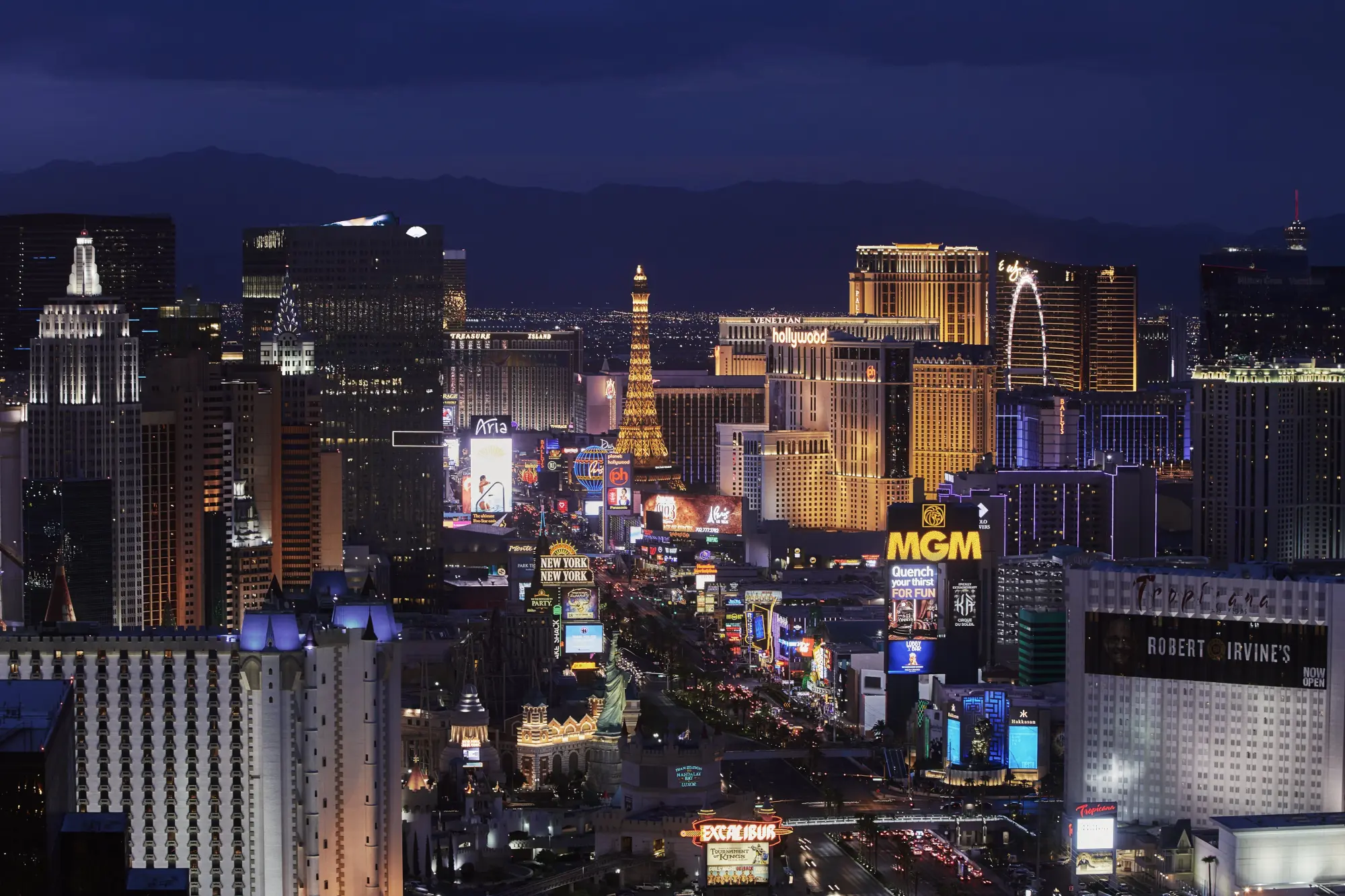 Dozens of famous Las Vegas Landmarks and signs, like Excalibur, MGM, and Paris Las Vegas, shine at night as thousands stroll below