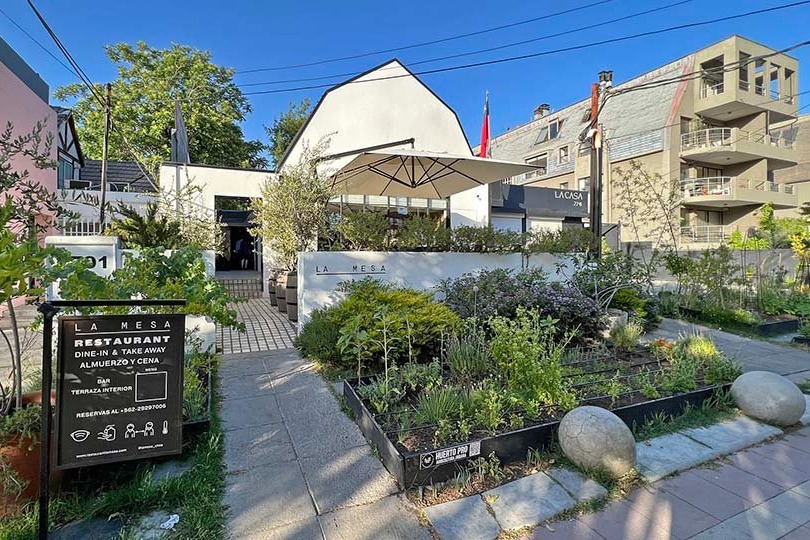 The exterior of La Mesa restaurant in Santiago, a modern white building with a garden and black signboard out front.