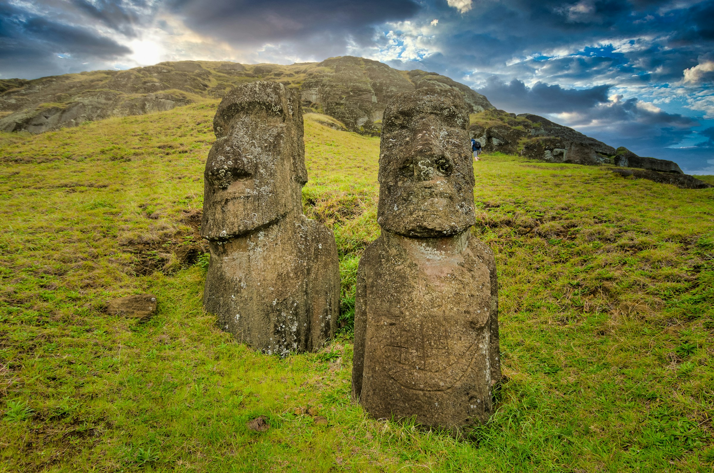 Stone Moai statues on a green hill at Rano Raraku in Rapa Nui with the sun peeking through the clouds.