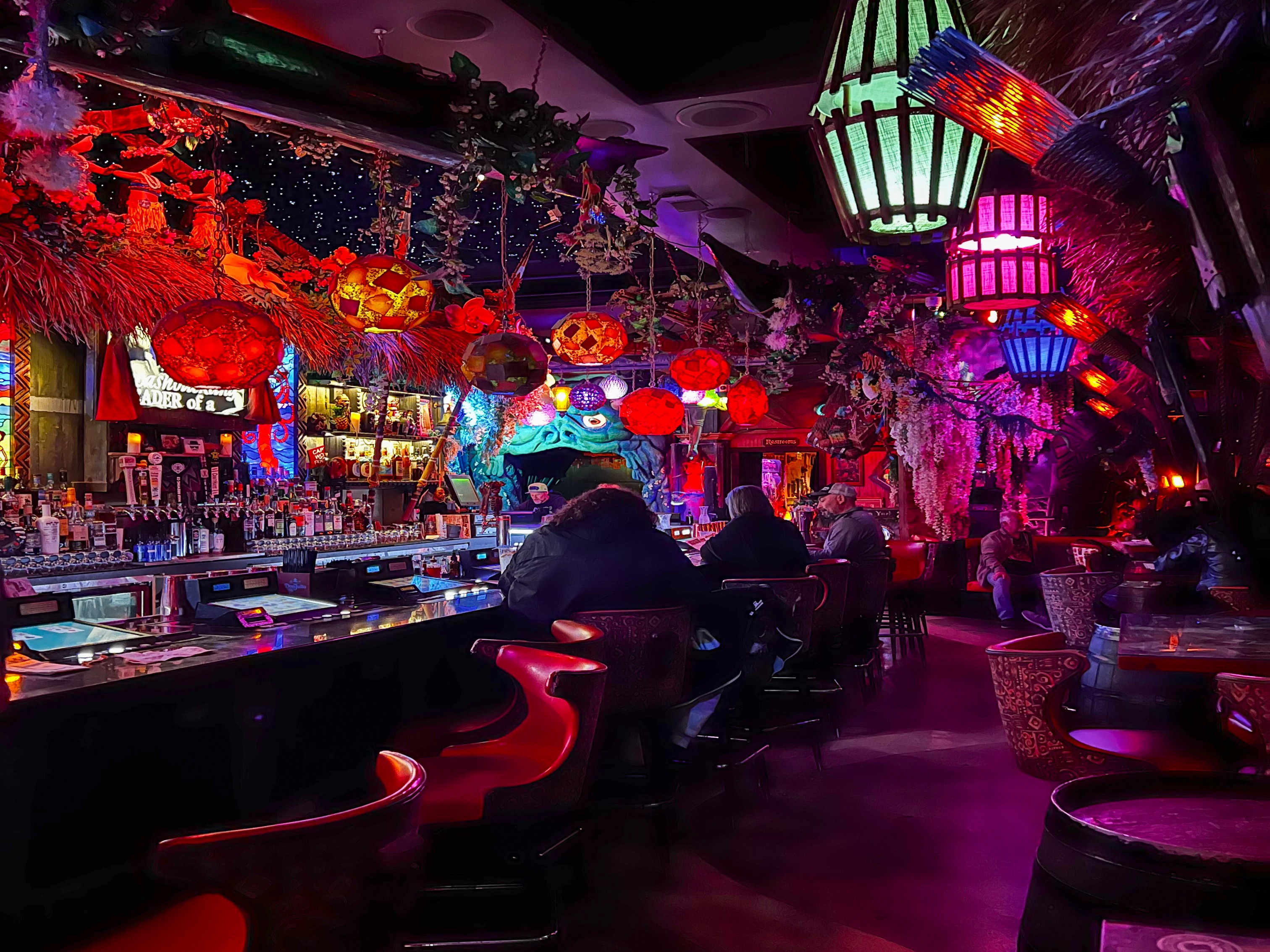 The image features a vibrant bar interior with eclectic decorations and colorful lighting, creating an inviting atmosphere.