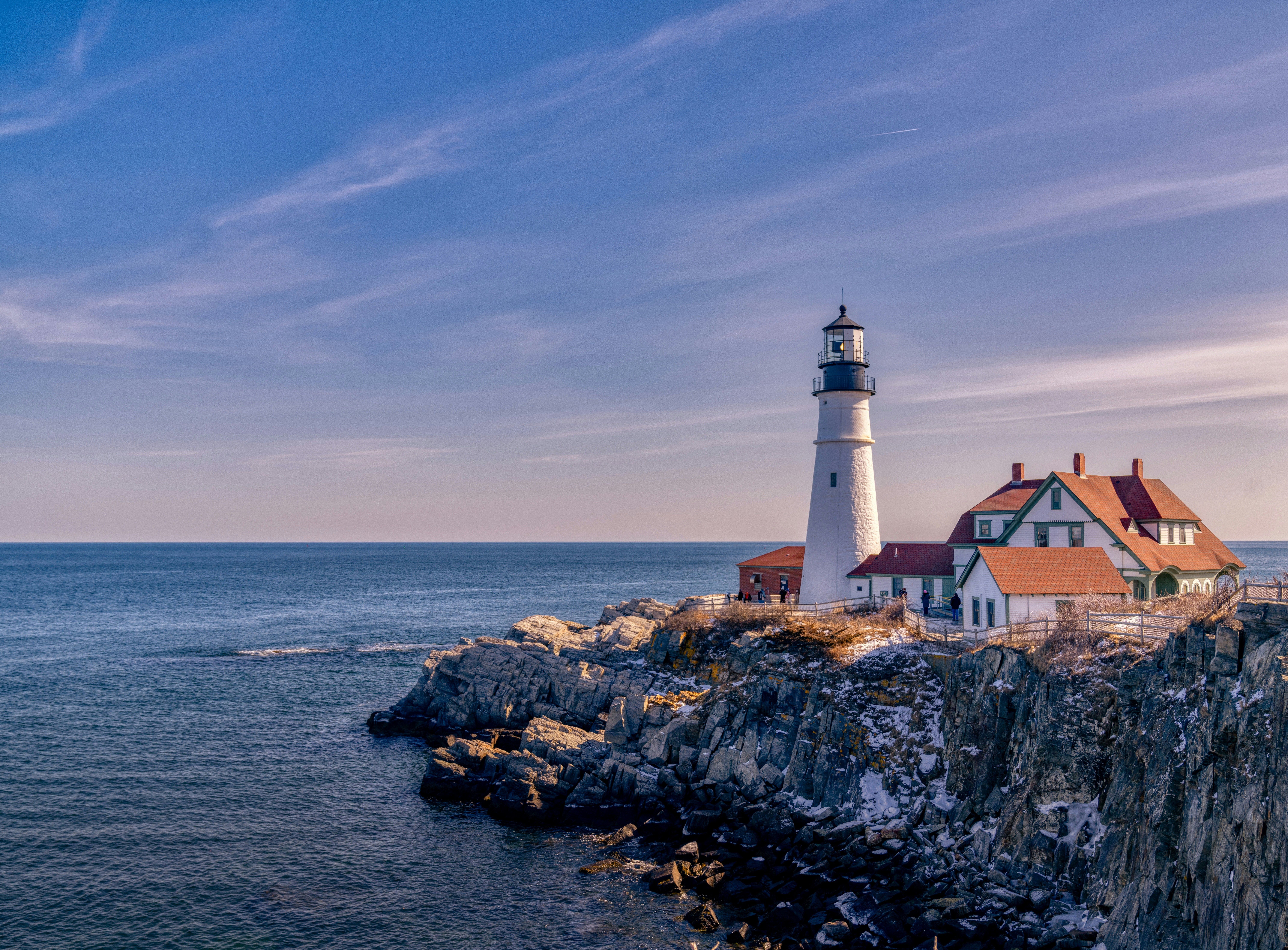 A lighthouse on the rocky coast of Portland Maine at twilight.