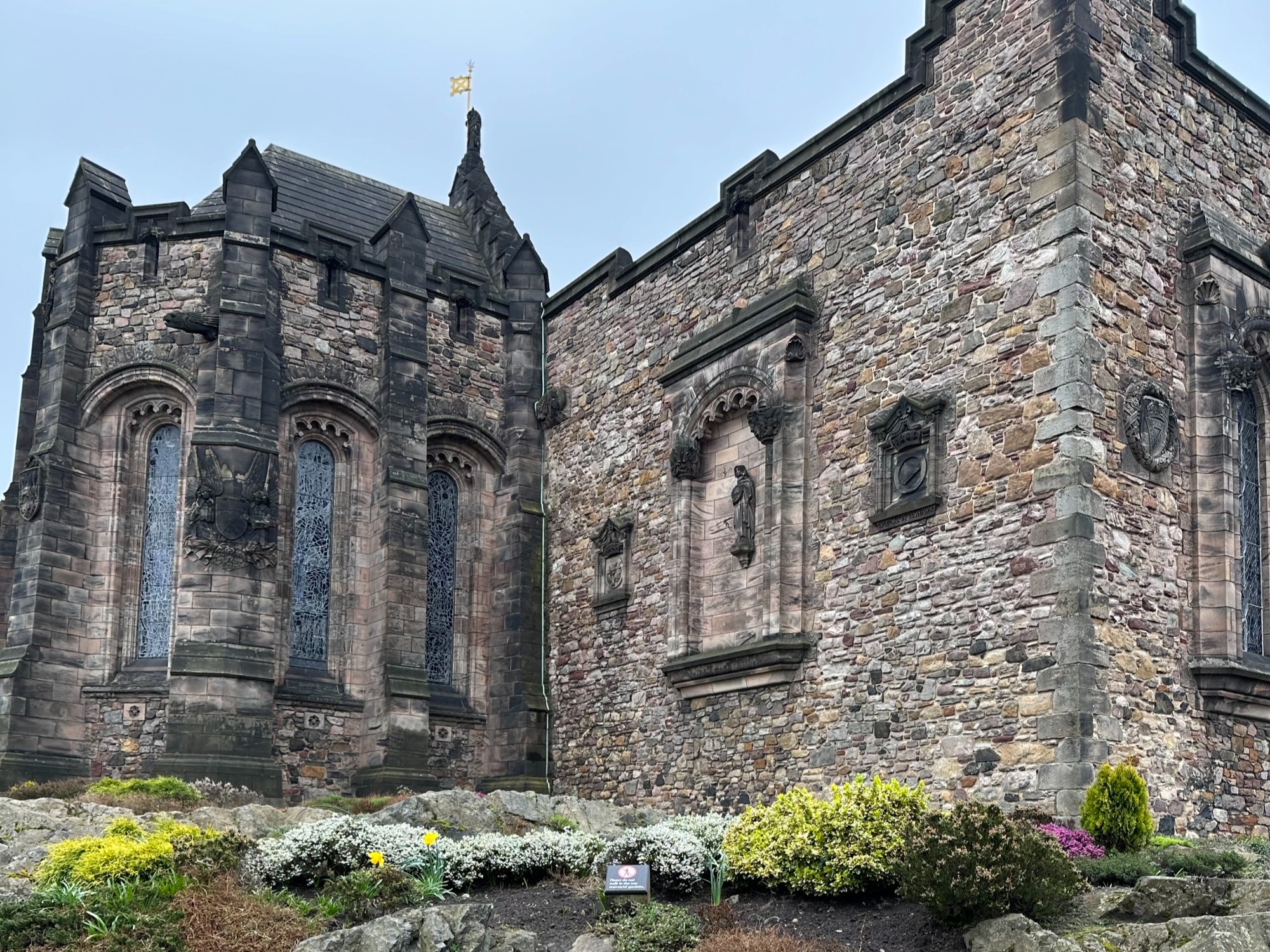 A view of a grand, stone castle with flowers and shrubs in front of it.