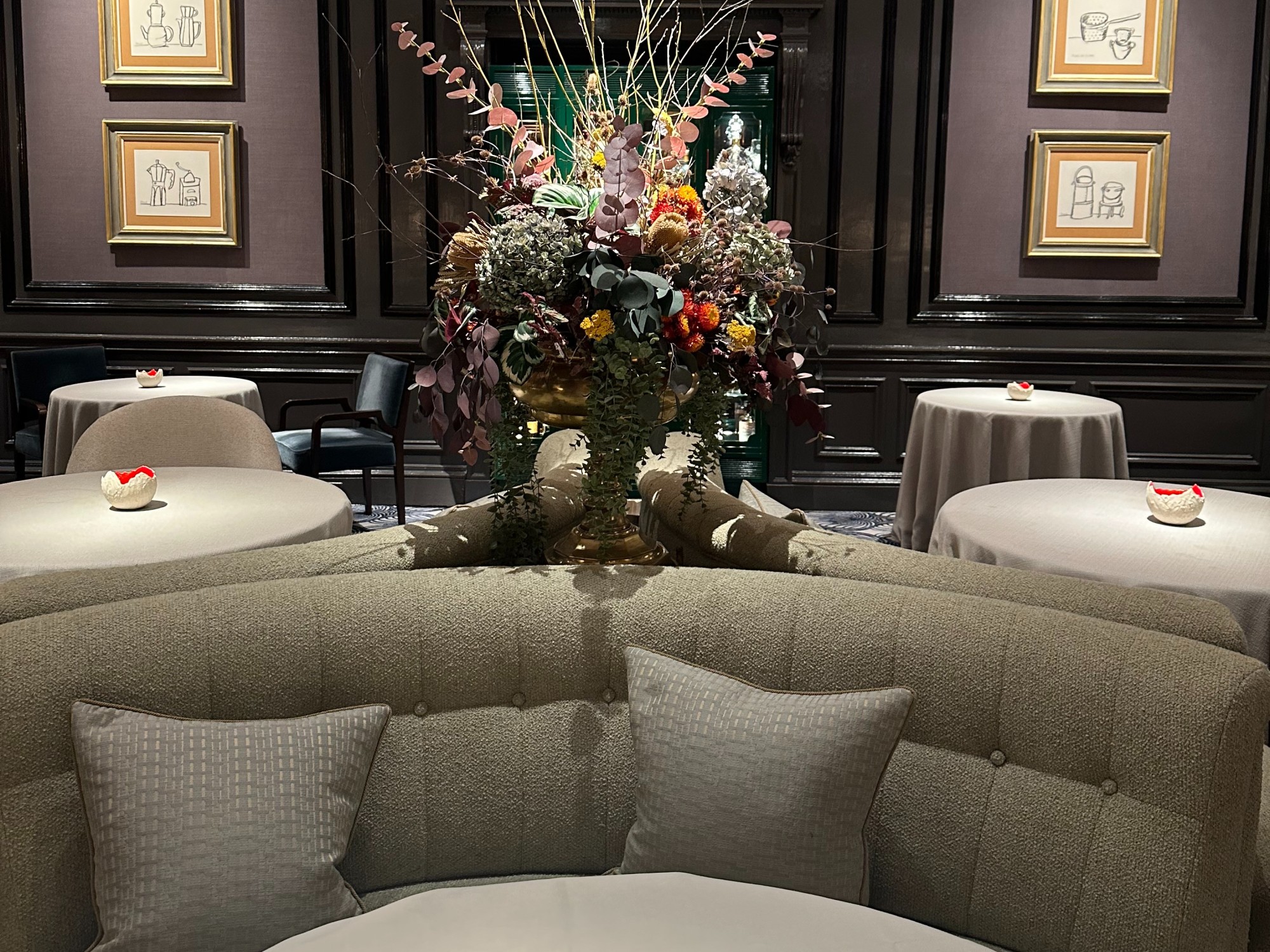 A lounge / dining area of a cozy booth, flowers, and small round tables.