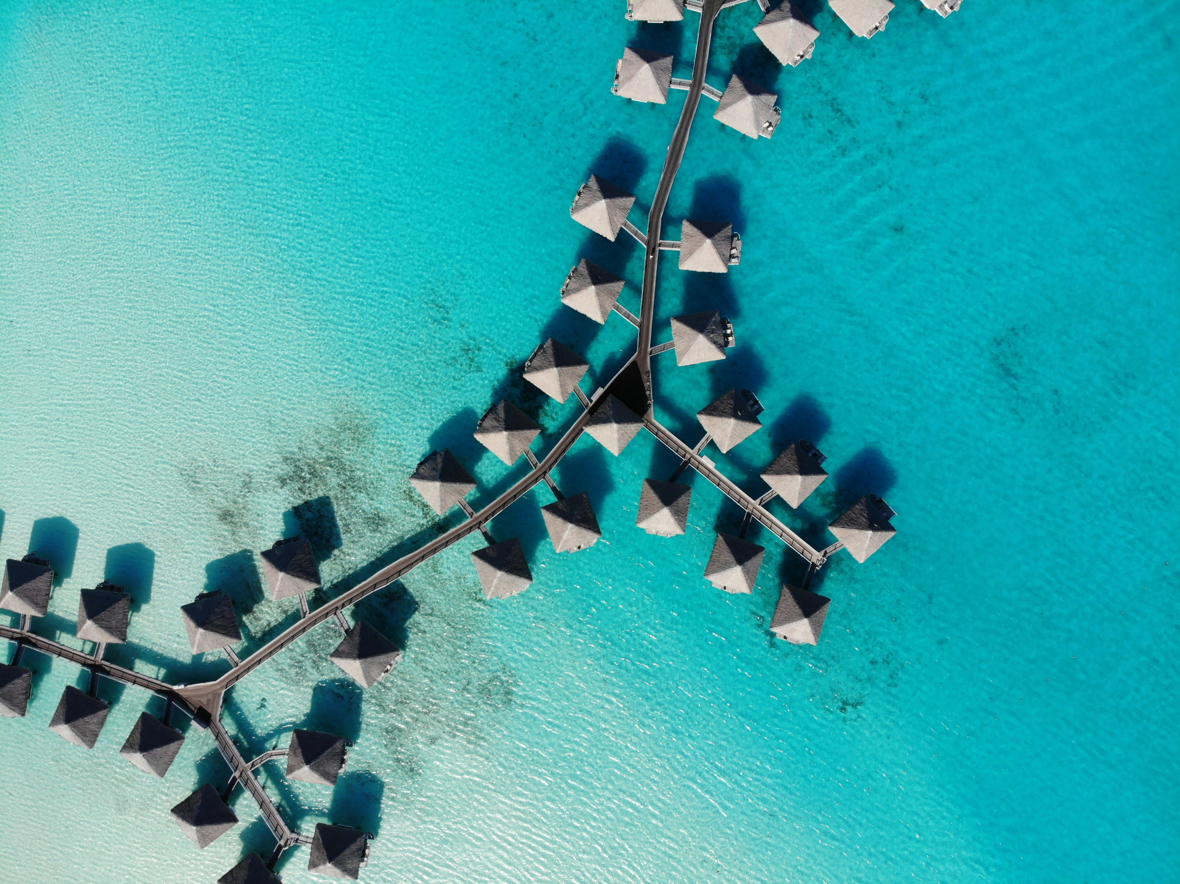 A drone view of a cluster of overwater bungalows in the crystal, clear sea.