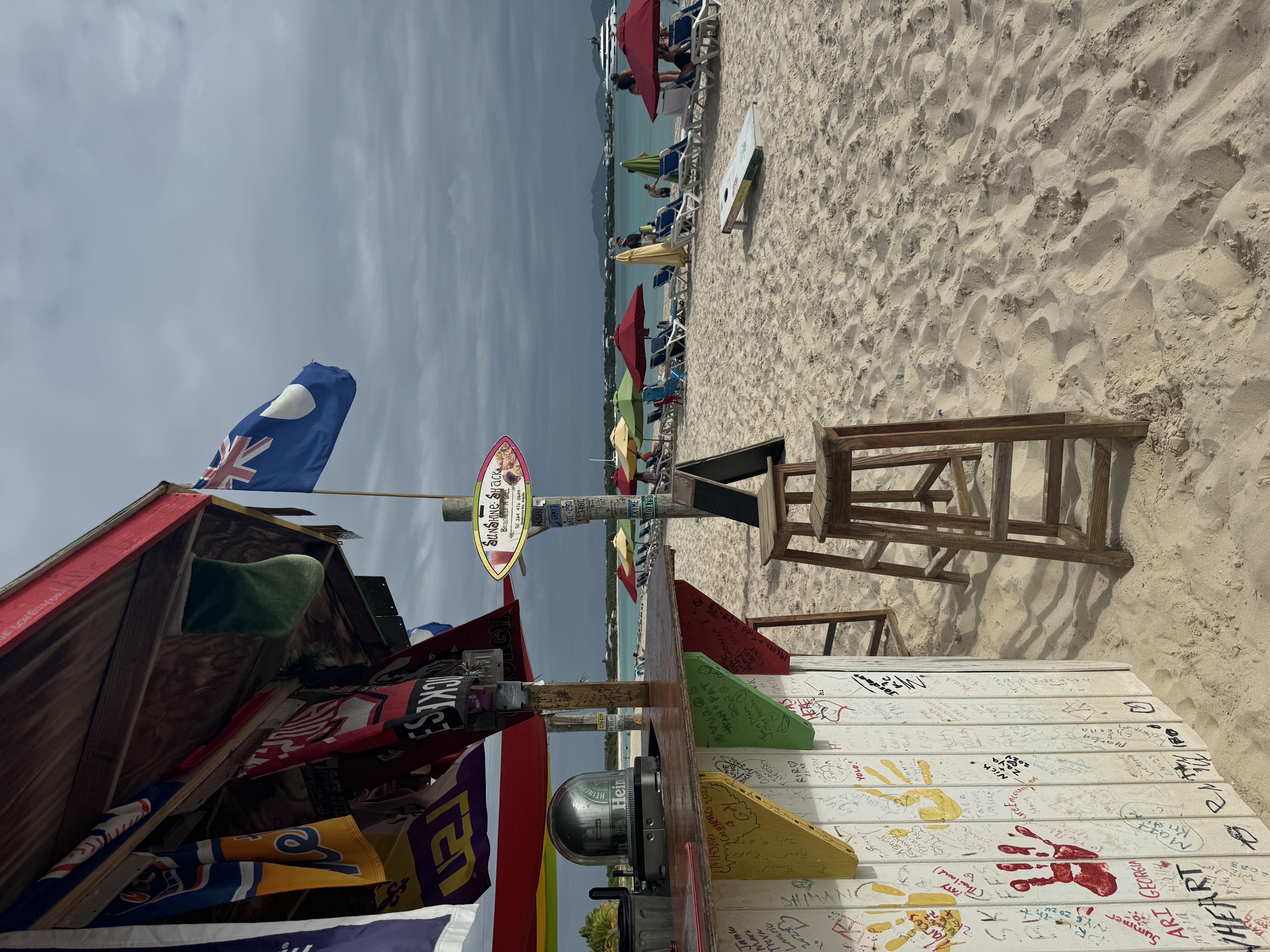 A view of a colorful beachside shack on a white sandy beach with people on sun loungers and a flag flying