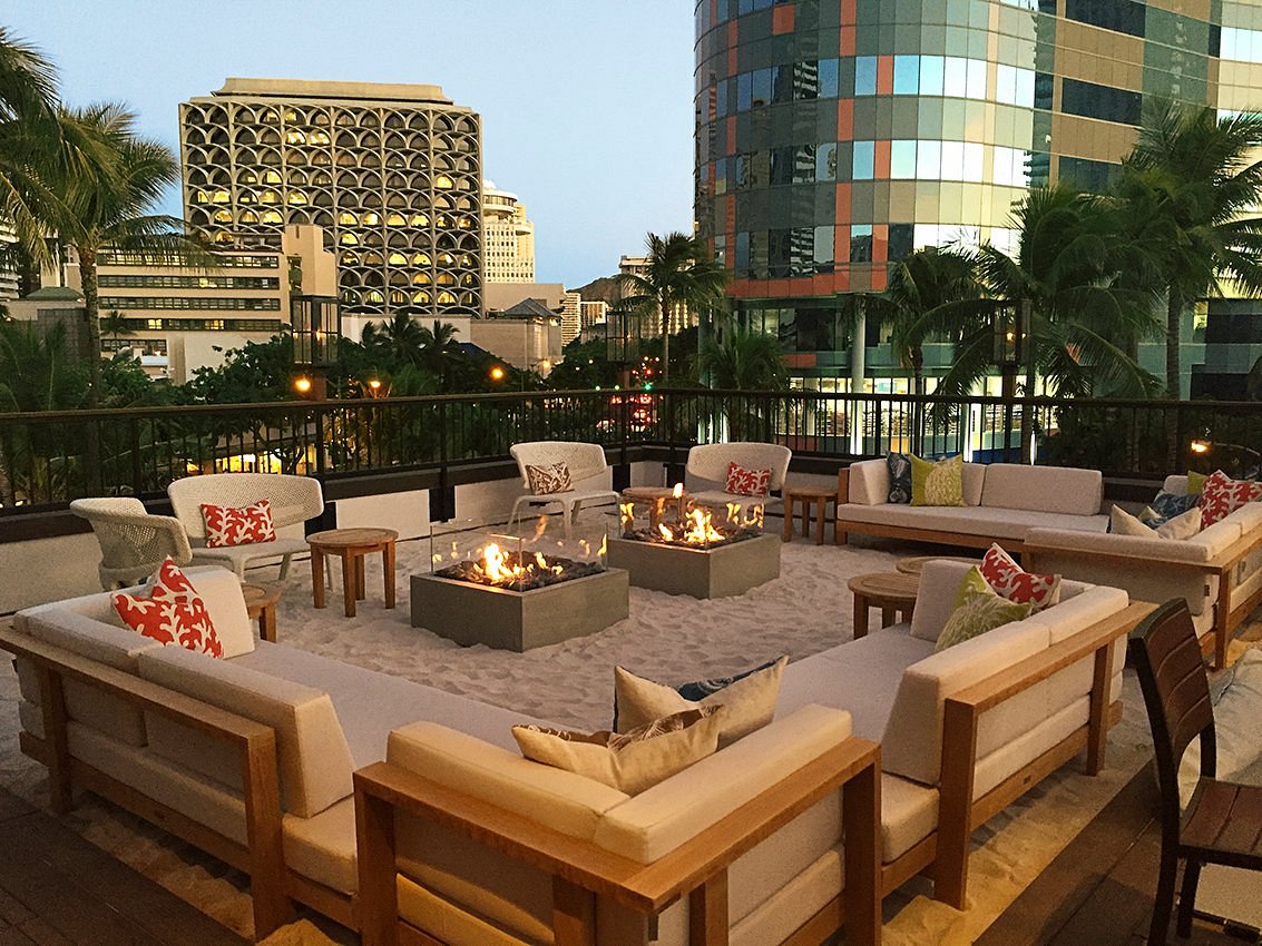 Outdoor lounge-area of chic couches on a manmade sandpit, with fireplaces.