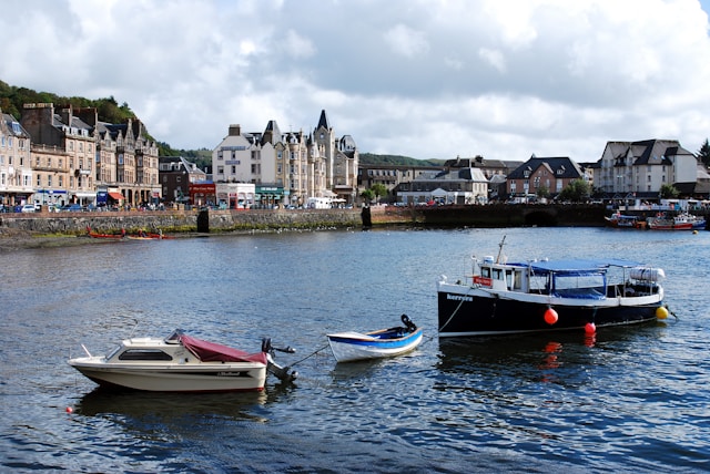 Small white, blue, and red boats on the water by the coastline, with buildings and houses in the background.