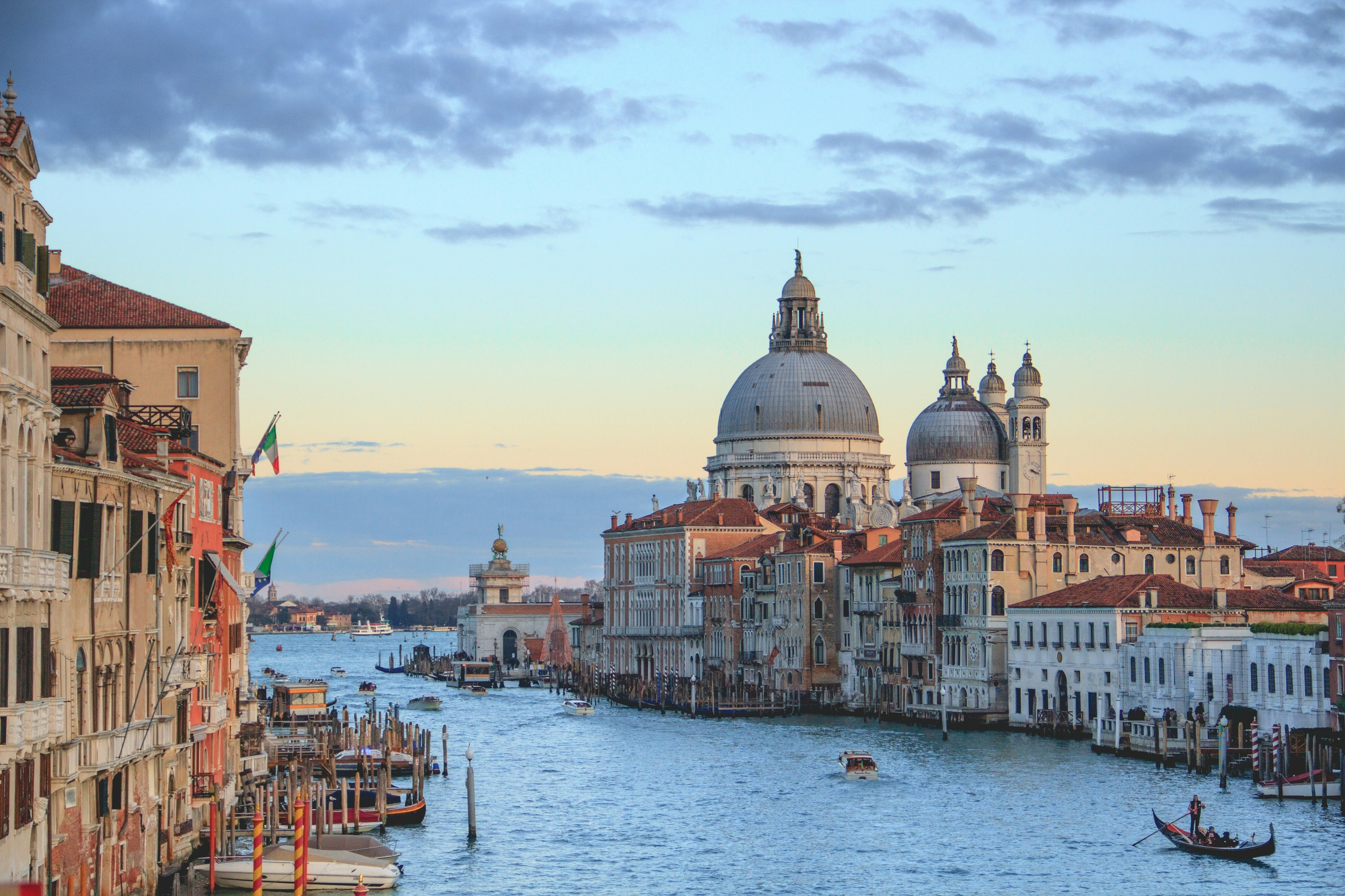 An aerial view of Venice, the canals and large domed buildings during the daytime. There is a light yellow sky with scattered clouds in the background.