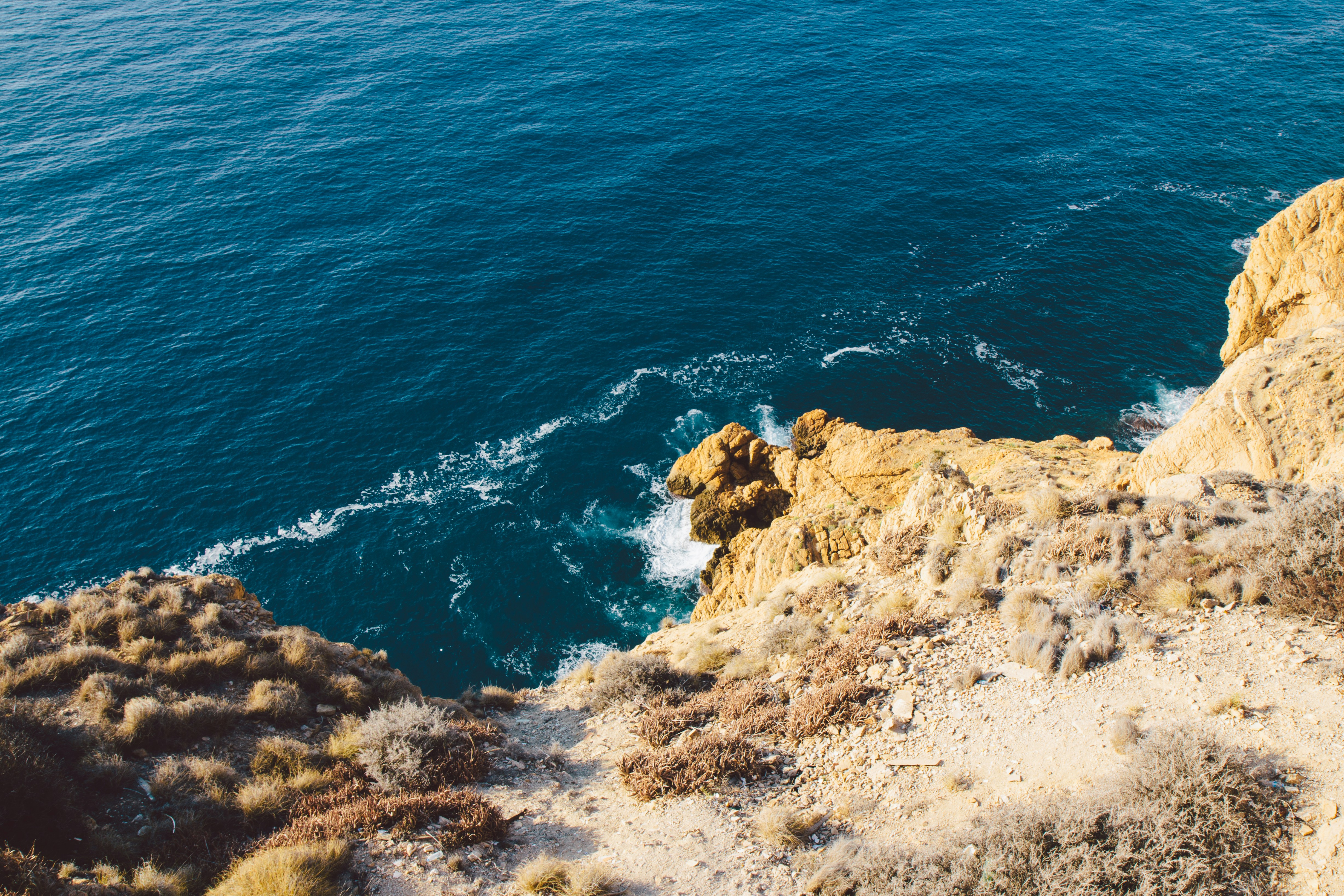 A view of the lake from a brown and rocky hill during the daytime.