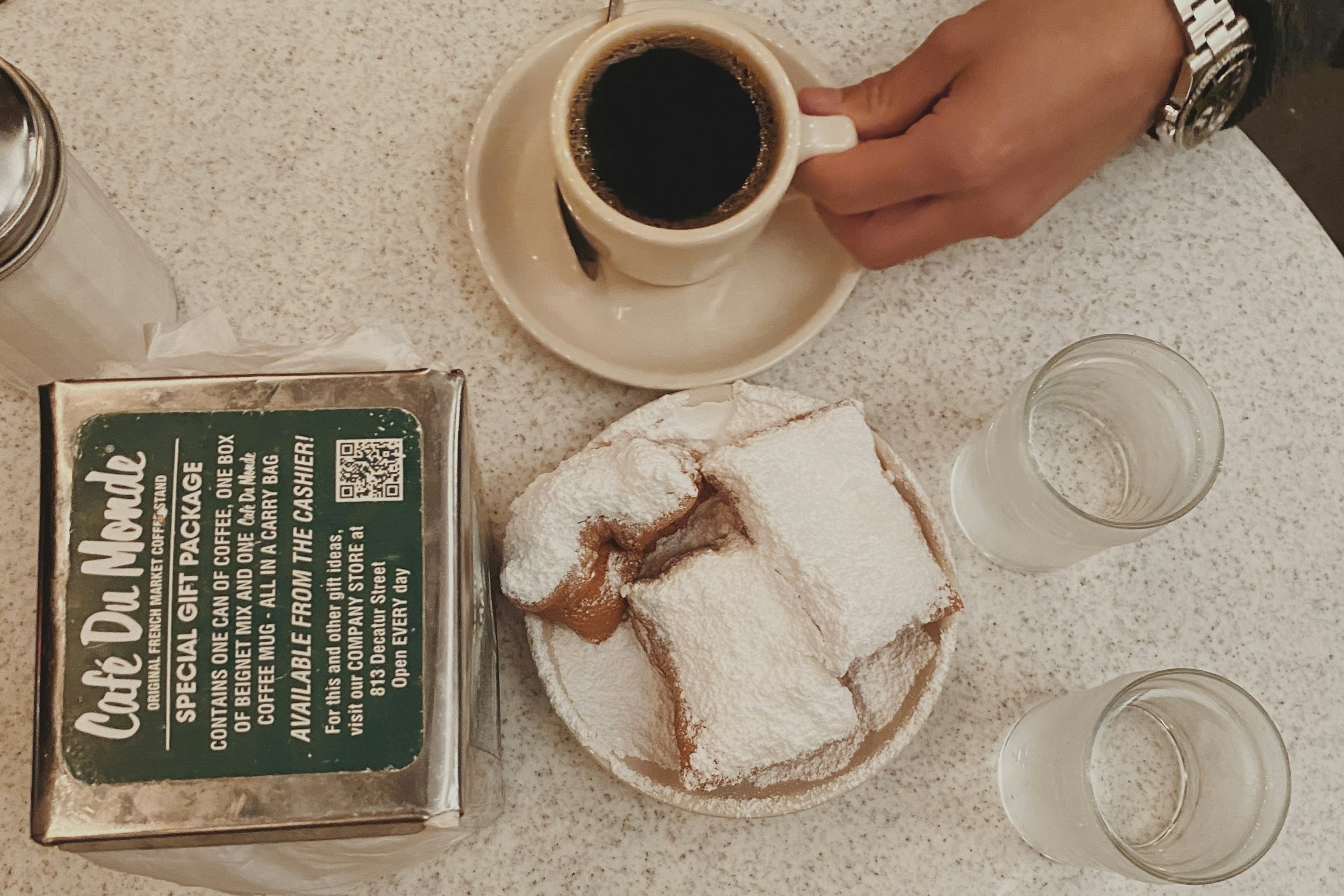 Three beignets on a plate next to a cup of coffee