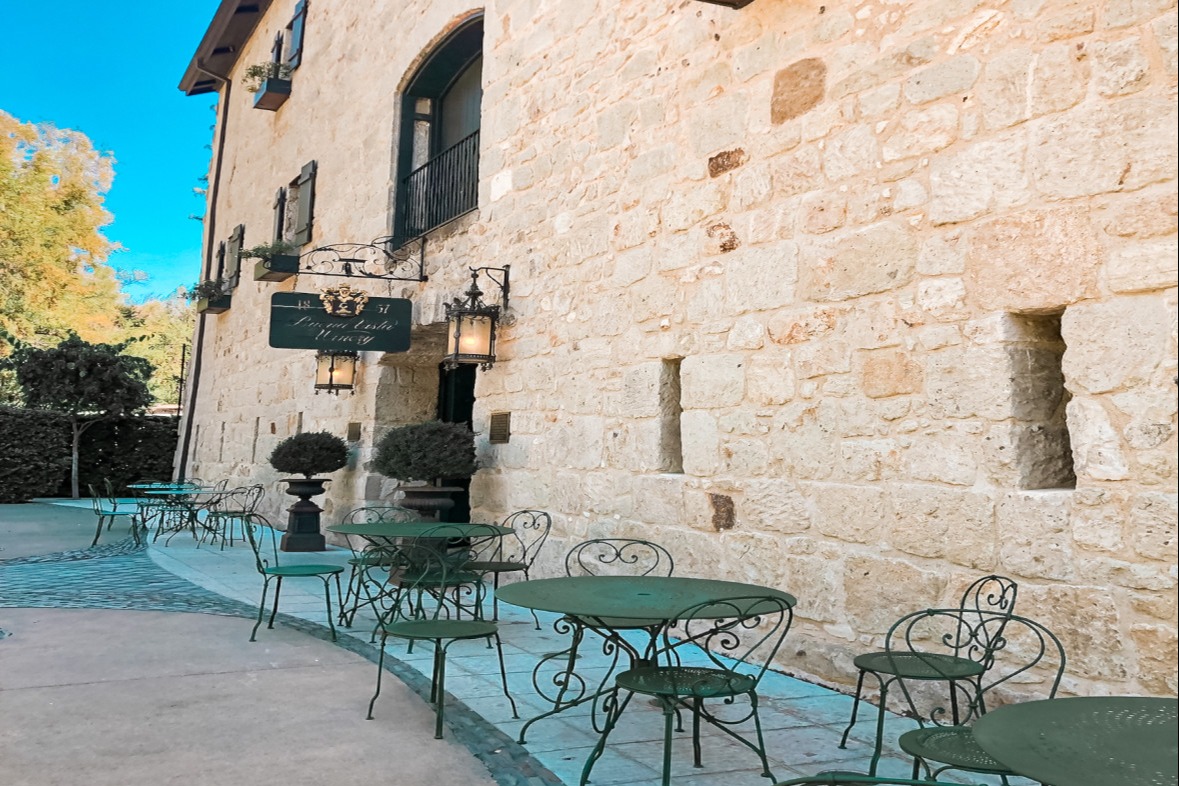 A picture of an outdoor winery with a stone exterior and iron tables and chairs