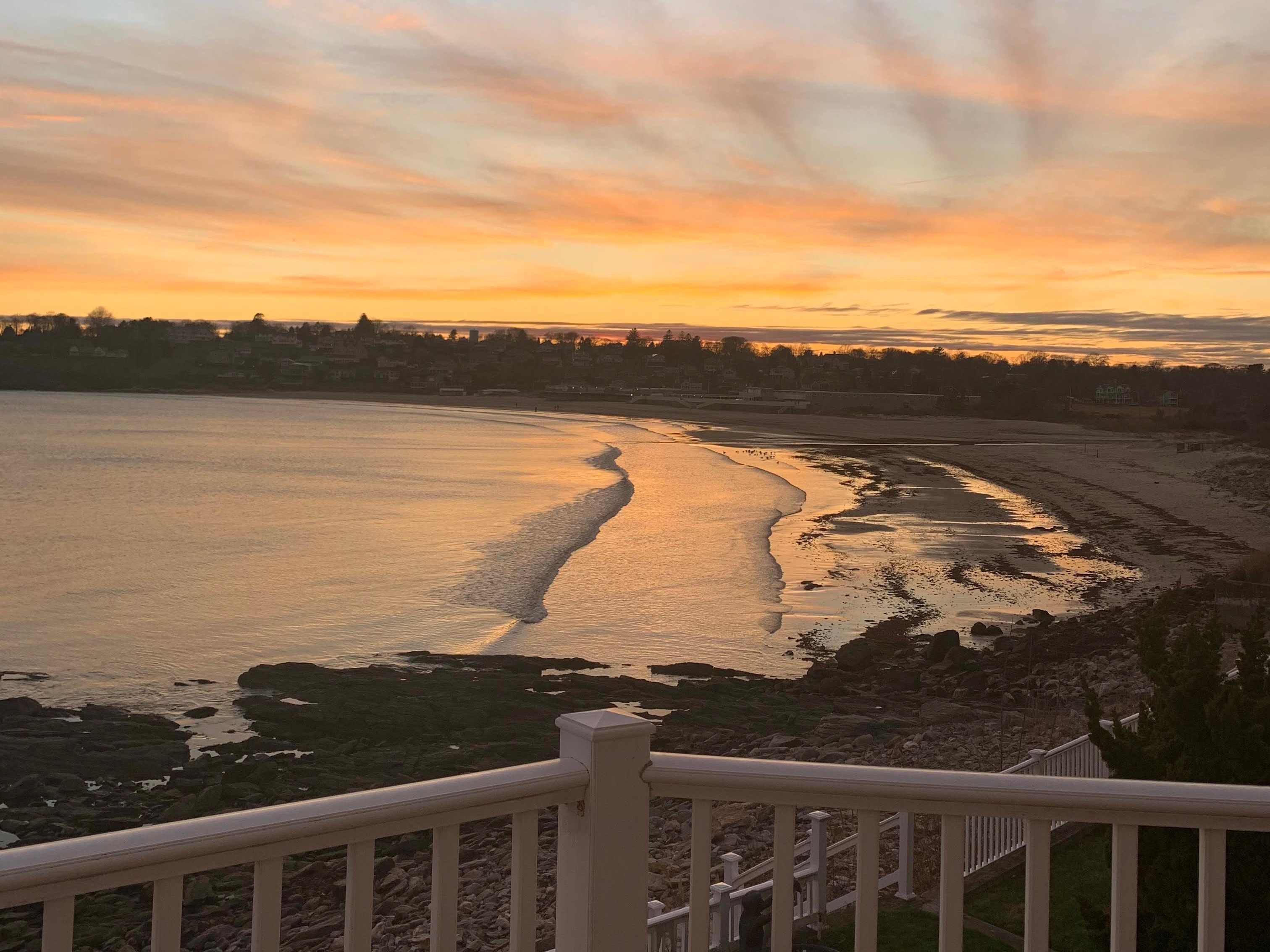 A tranquil sunset over a calm sea, viewed from a white balcony, with the sky and water bathed in warm, enchanting colors.