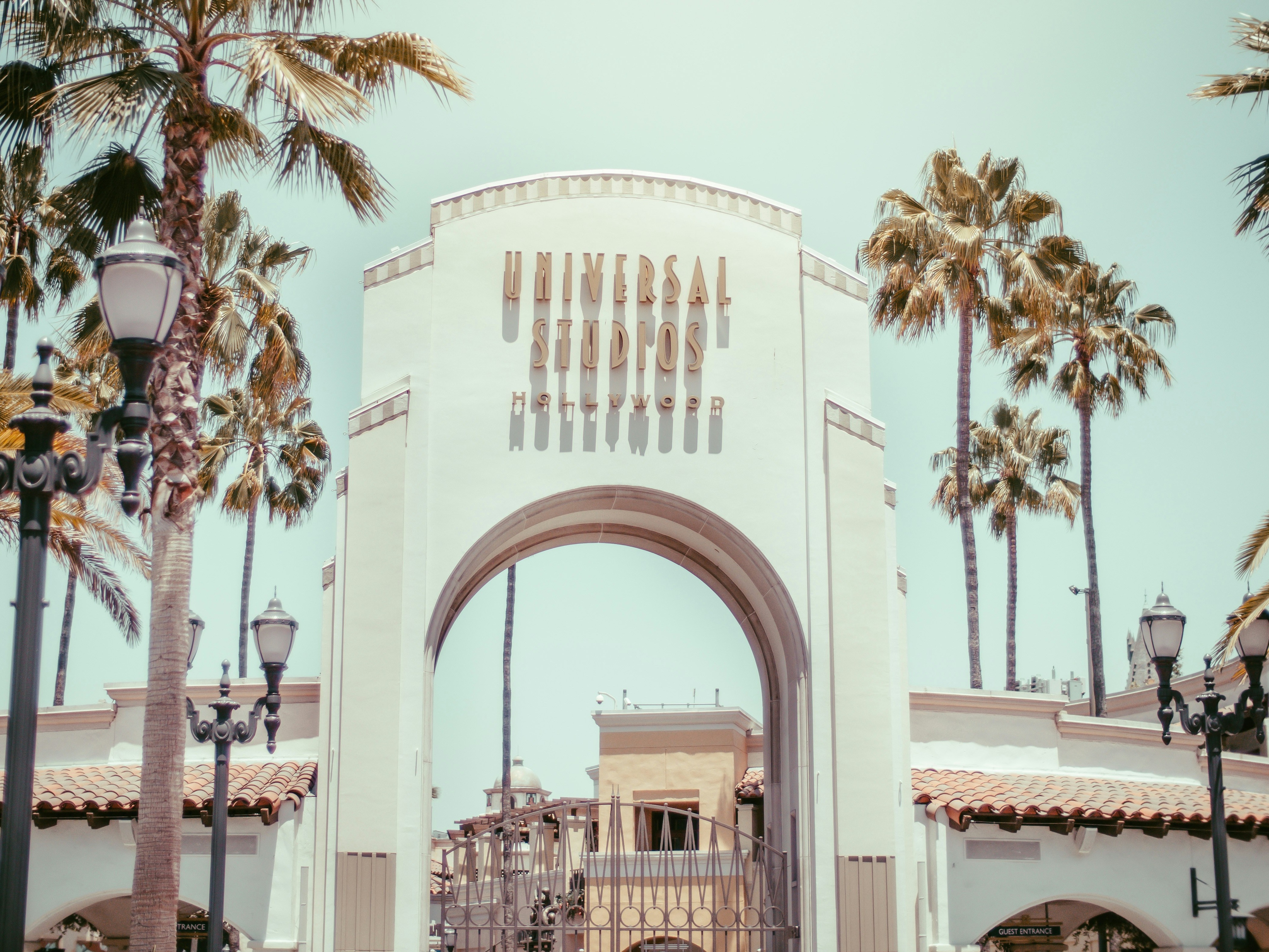 A white arched entrance to Hollywood's Universal Studios in North Hollywood on a sunny California day, surrounded by palm trees.