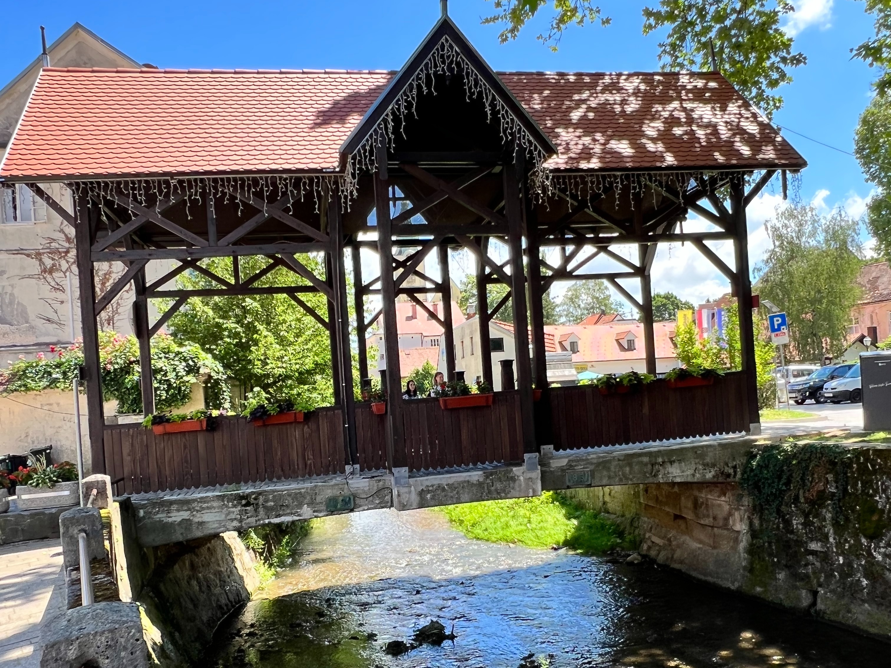 A view of an old bridge with red roofing, wooden paneling, and a creek beneath it.
