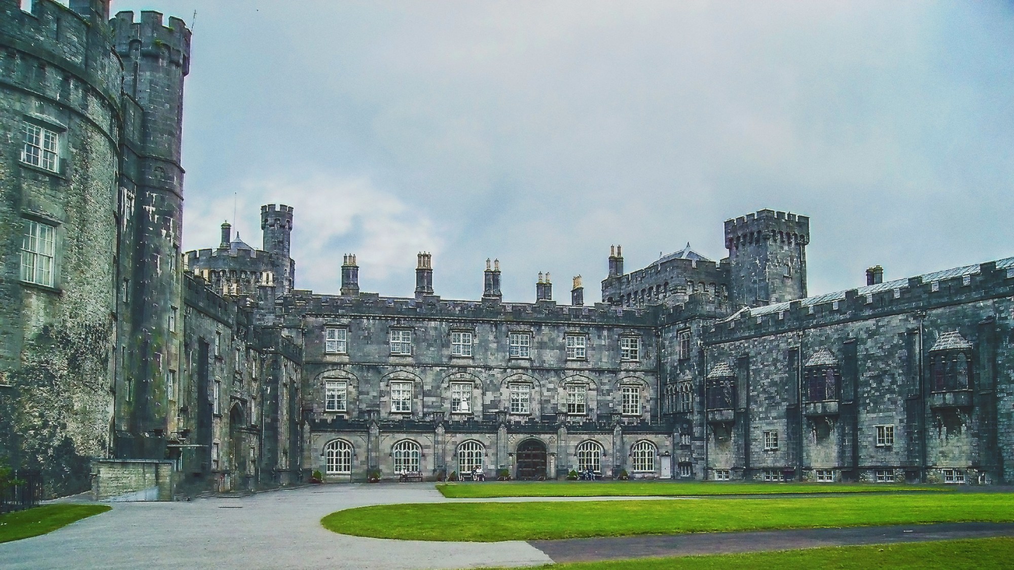 A large old and grey stone castle with a green lawn in front of it.