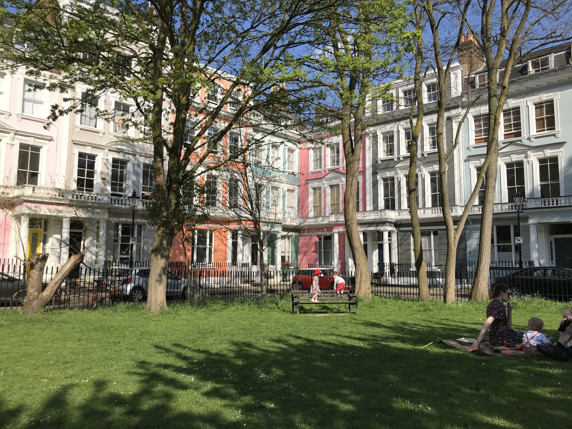 Small park in front of London houses with families sitting on the grass