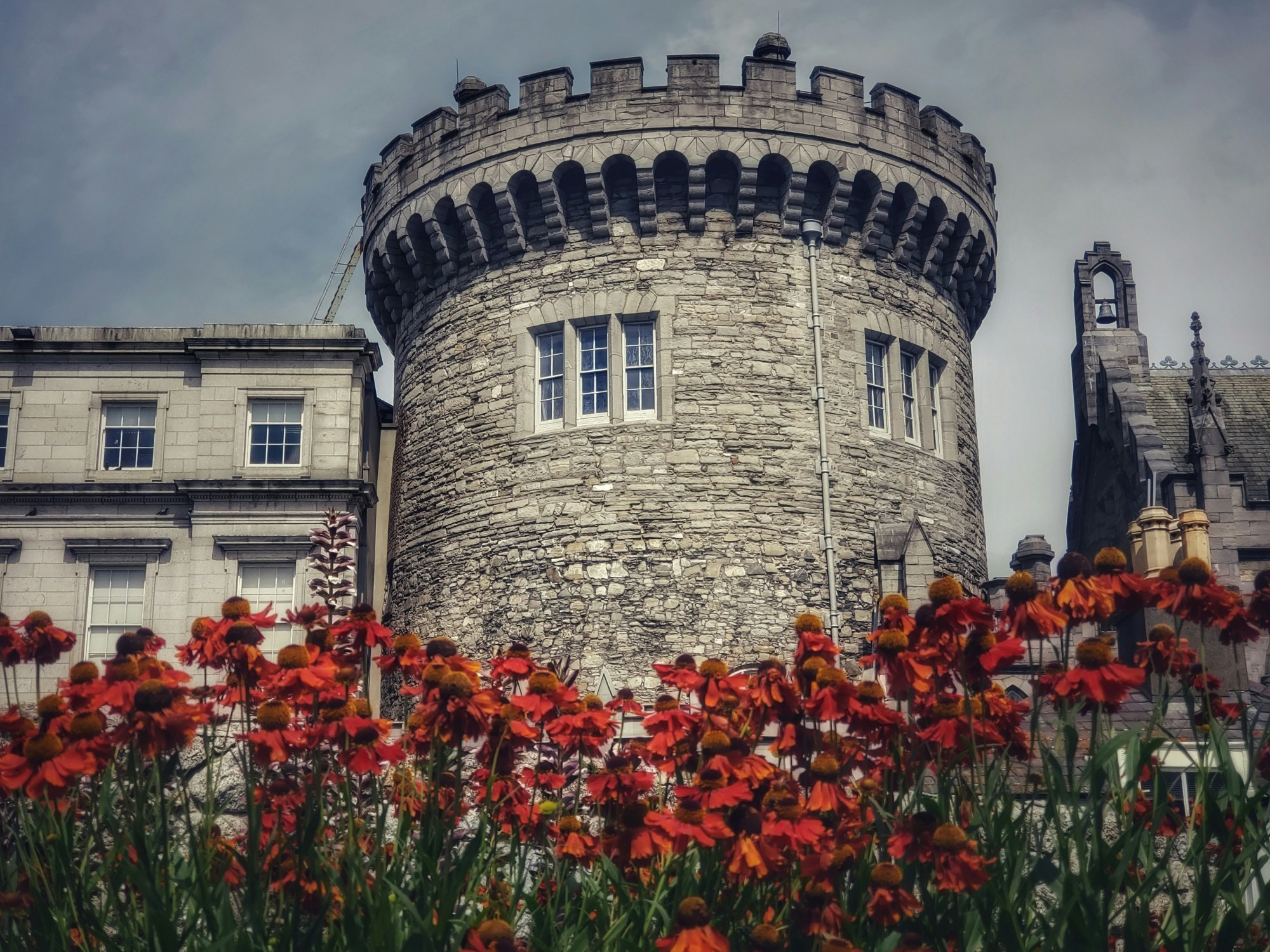 A grey castle behind an assortment of red flowers.