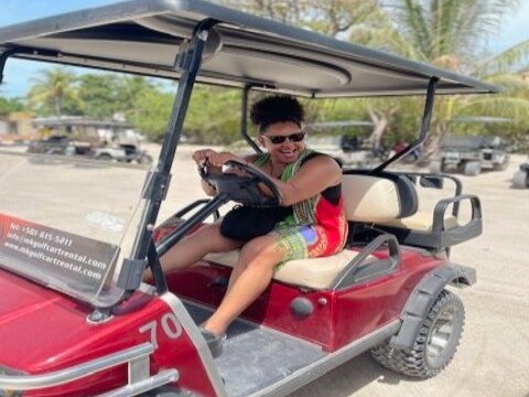 A woman riding a red golf cart near the beach during daytime.