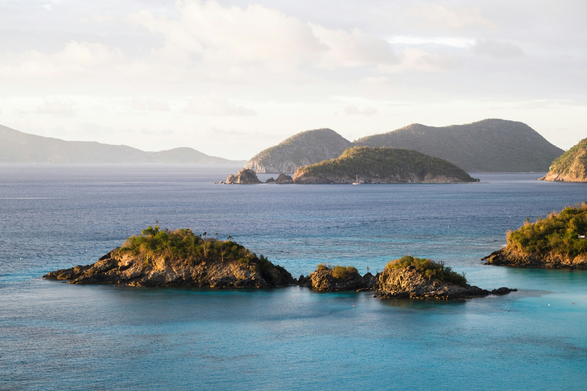 A view of the blue sea with various isles and mountains covered in rock and trees in the surrounding areas.