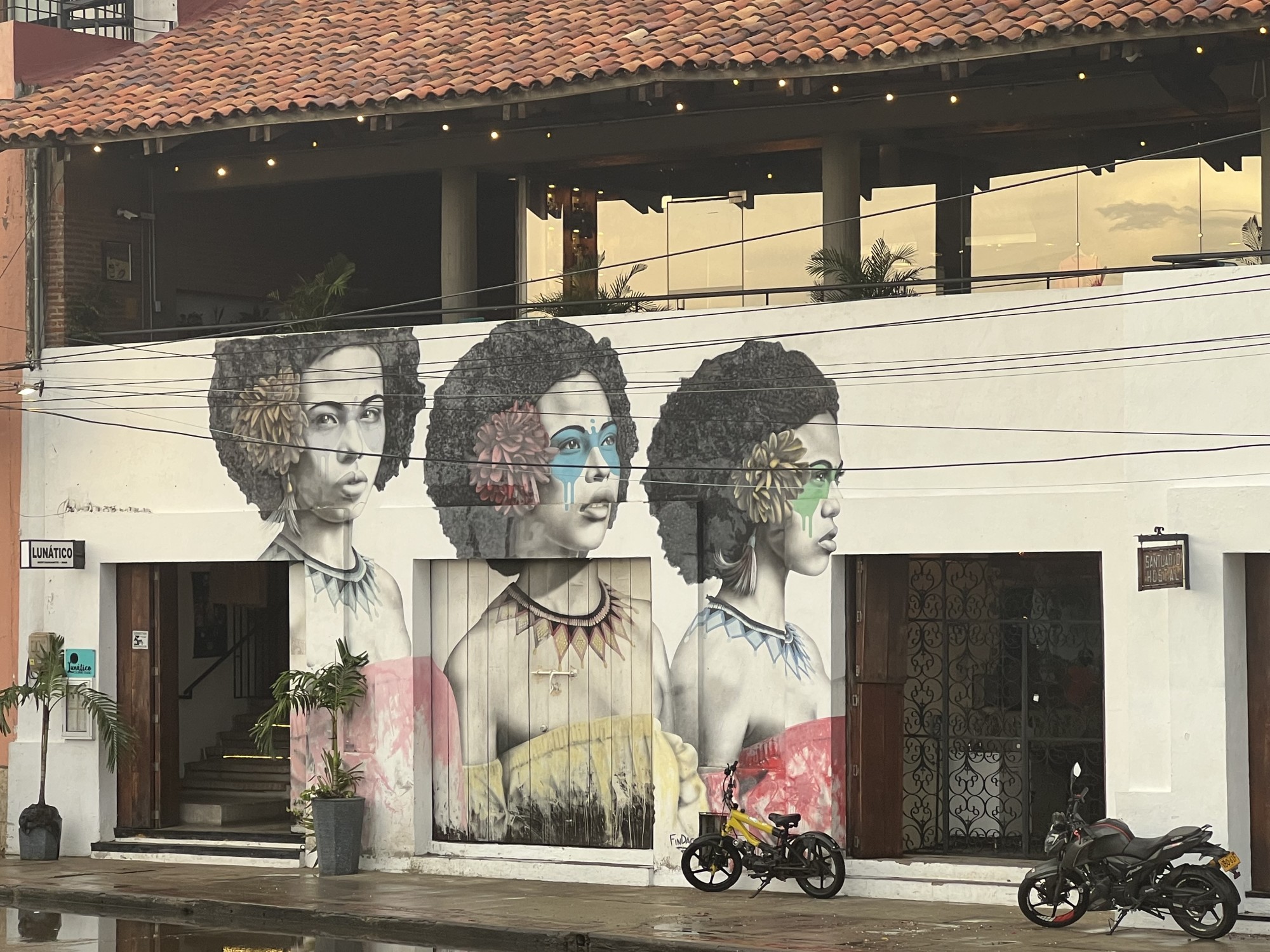 A mural of three women against a white building with a terracotta roof.