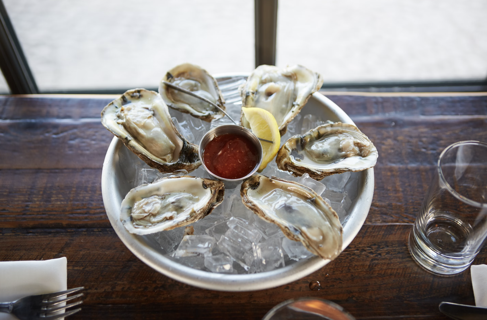 A plate of oysters on ice, positioned on top of a wooden table.