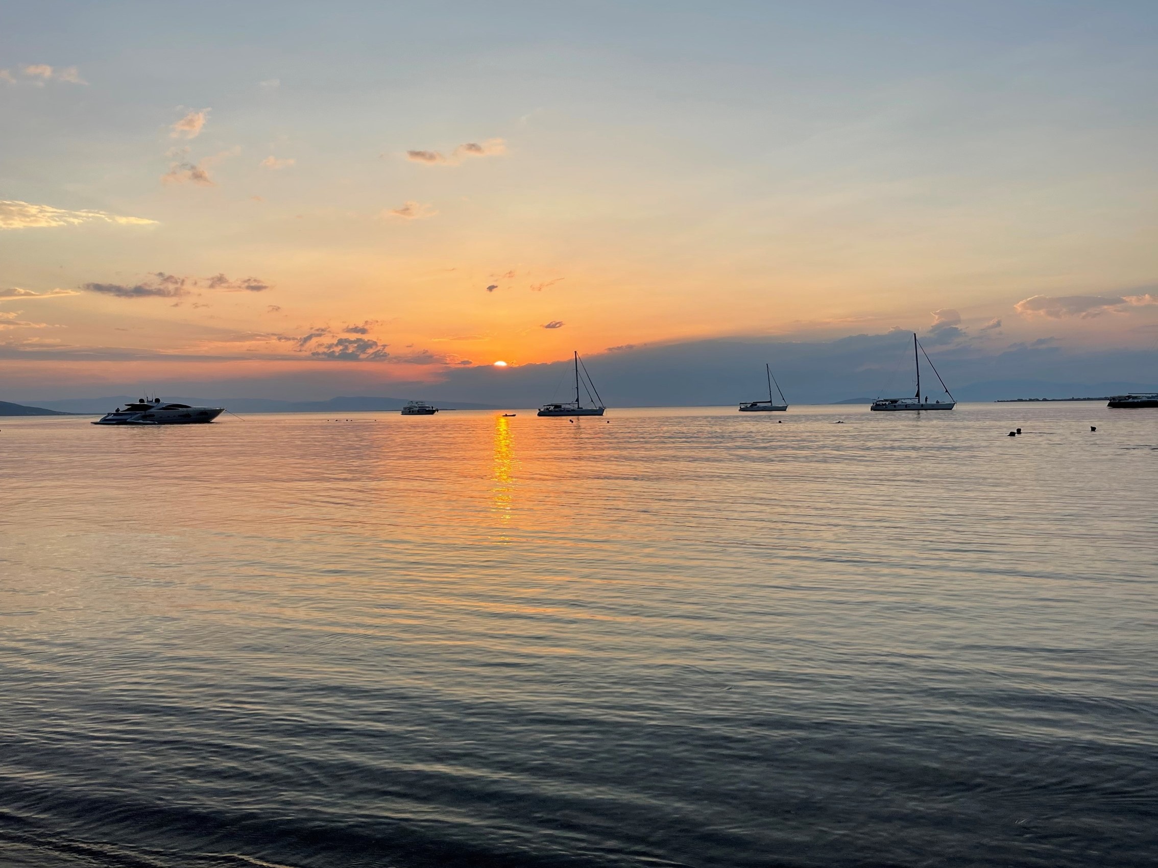 A picture of the sea with some boars sailing at sunset.