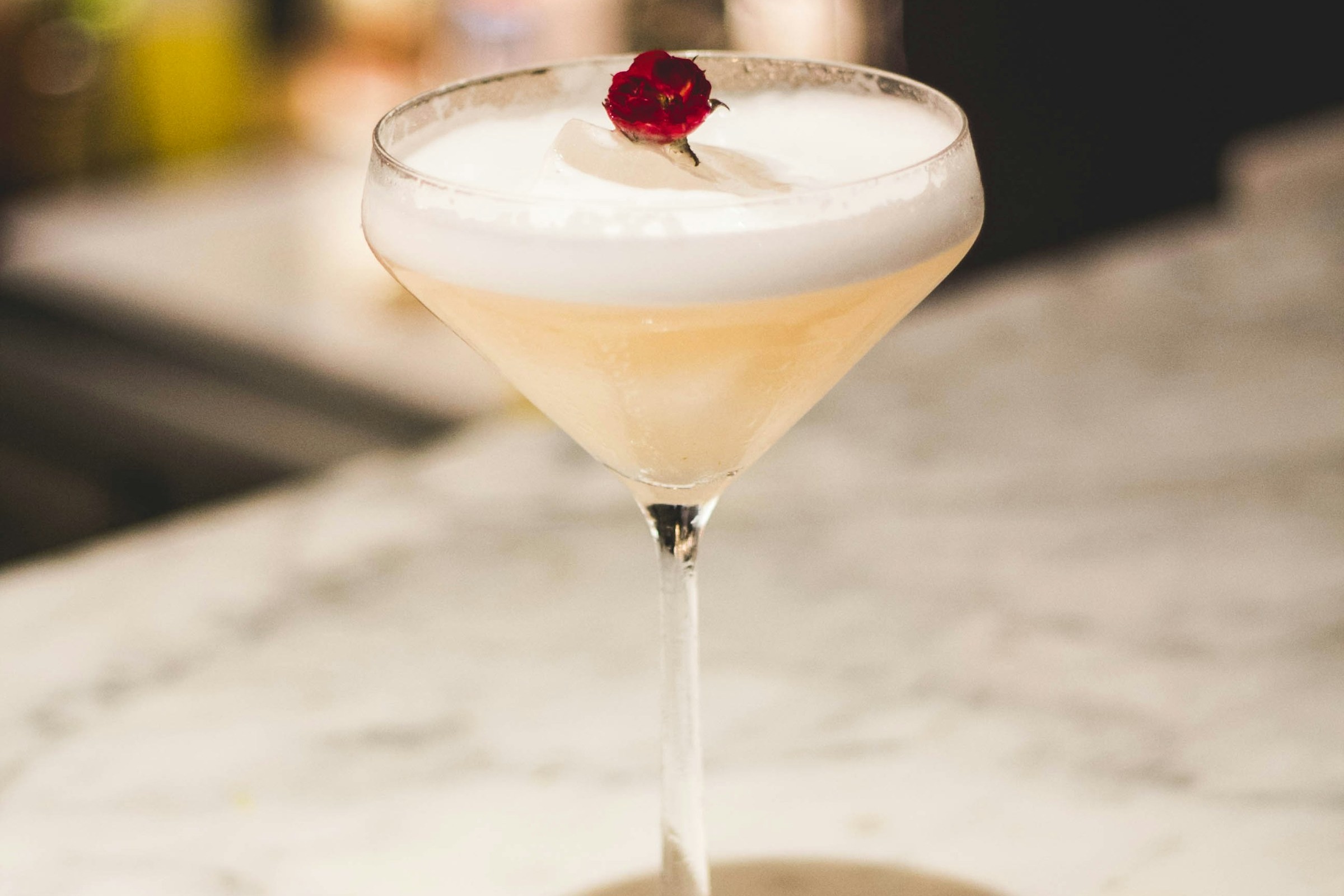 A drink with foam and a small red flower from Death & Co.