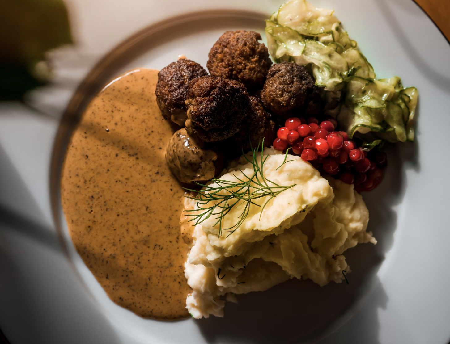 A plate of Swedish meatballs, mashed potatoes, lingonberries, greens and gravy.