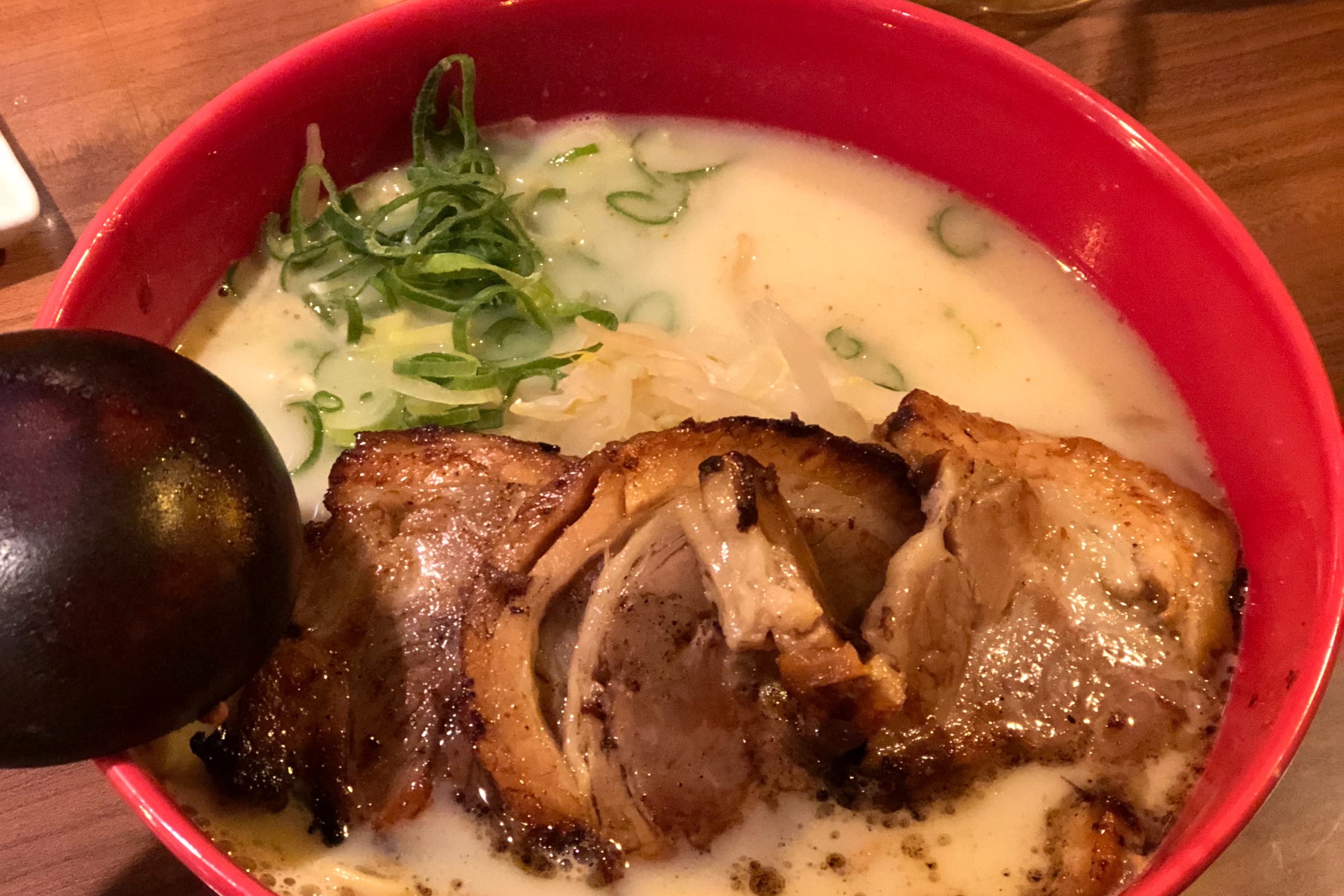 A bowl of ramen with a thick broth, greens and meat.