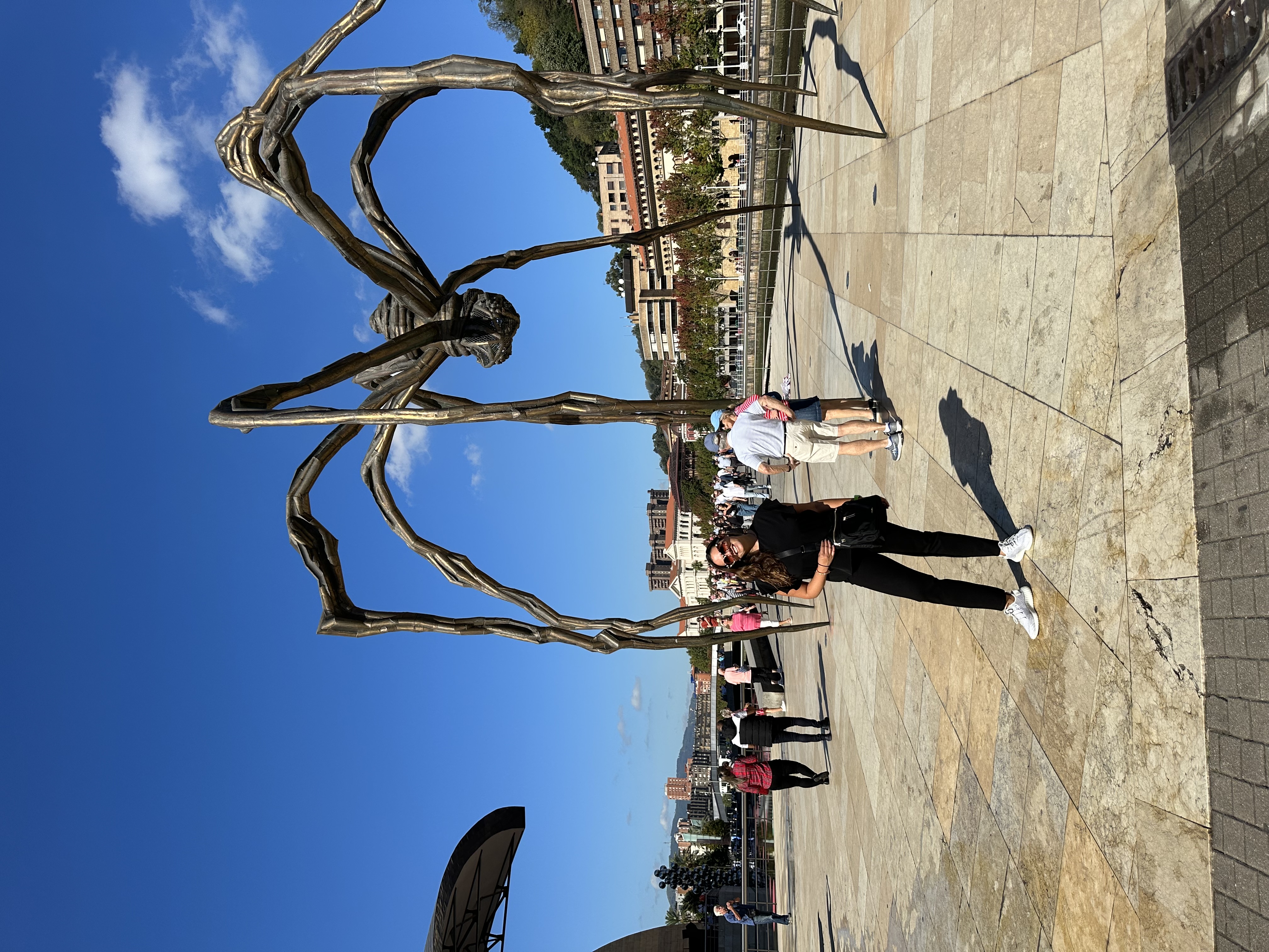 Travel advisor Andrea posing in front of Maman spider-shaped sculpture with other people in view on a sunny day