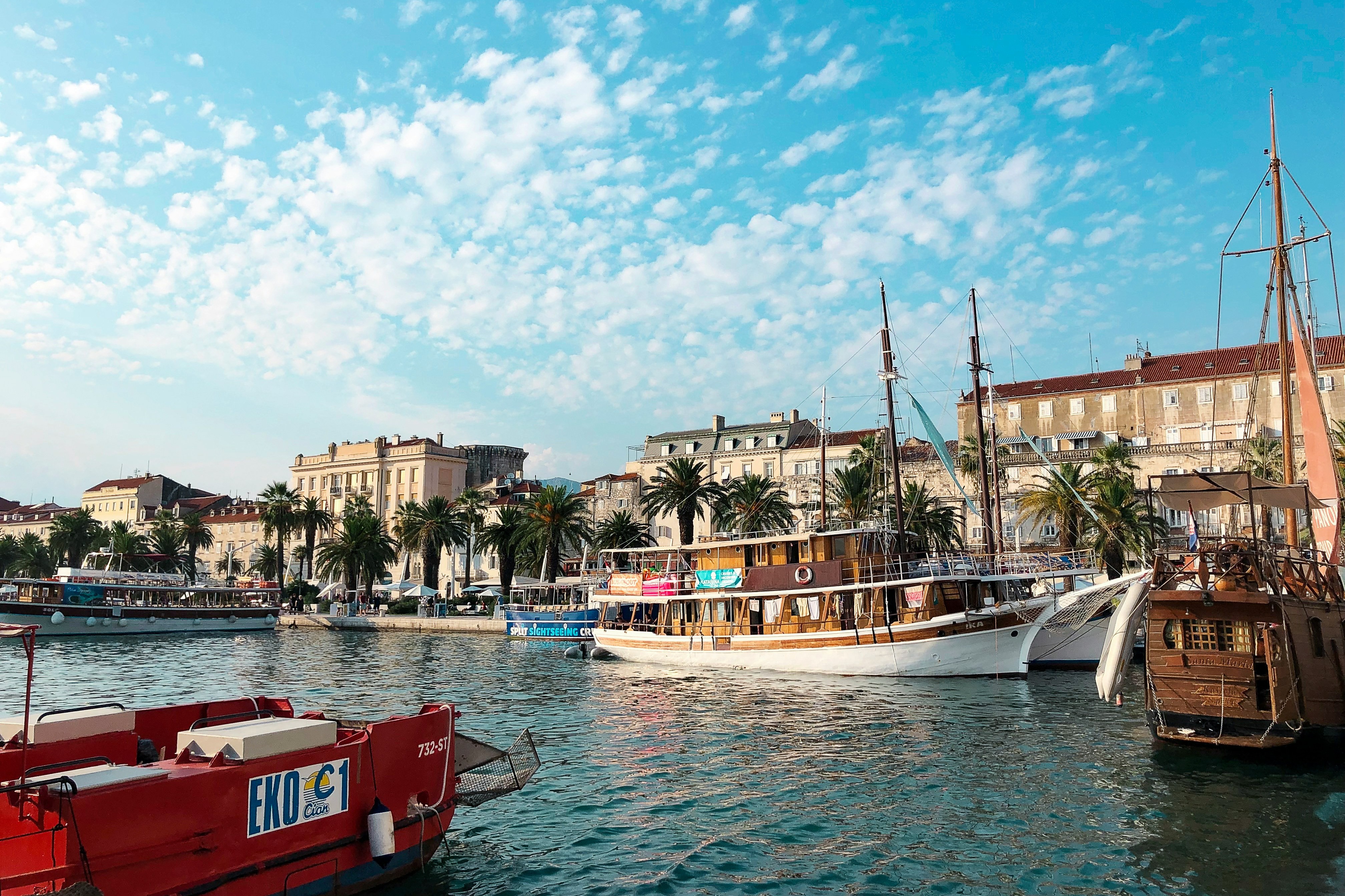 A picture of red and white colored boats on the water anchored near the buildings during the daytime.