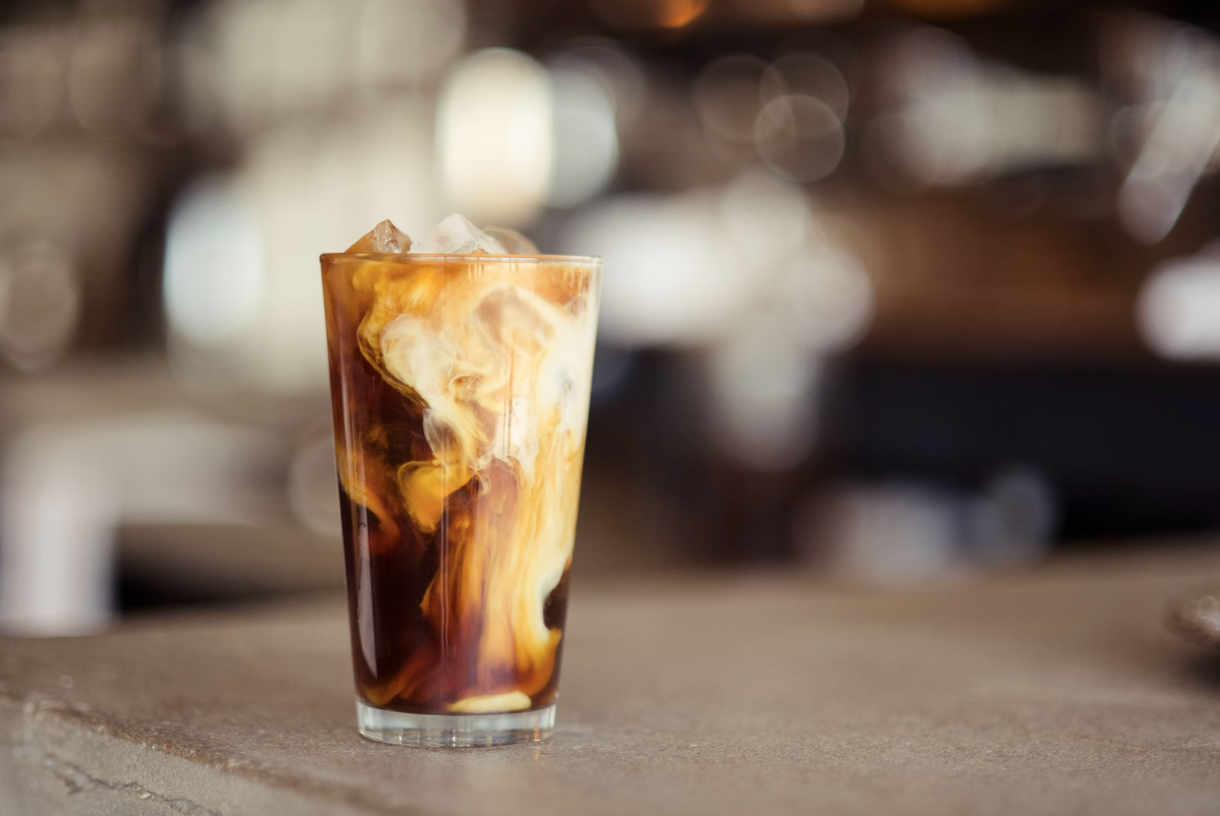 A glass of iced coffee with white swirls inside of it.