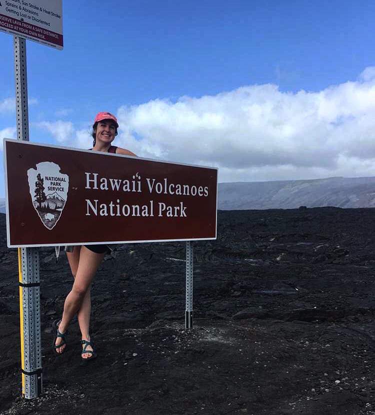 Travel advisor Rachel standing on a dark gray surface by a Hawaii Volcanoes National Park sign