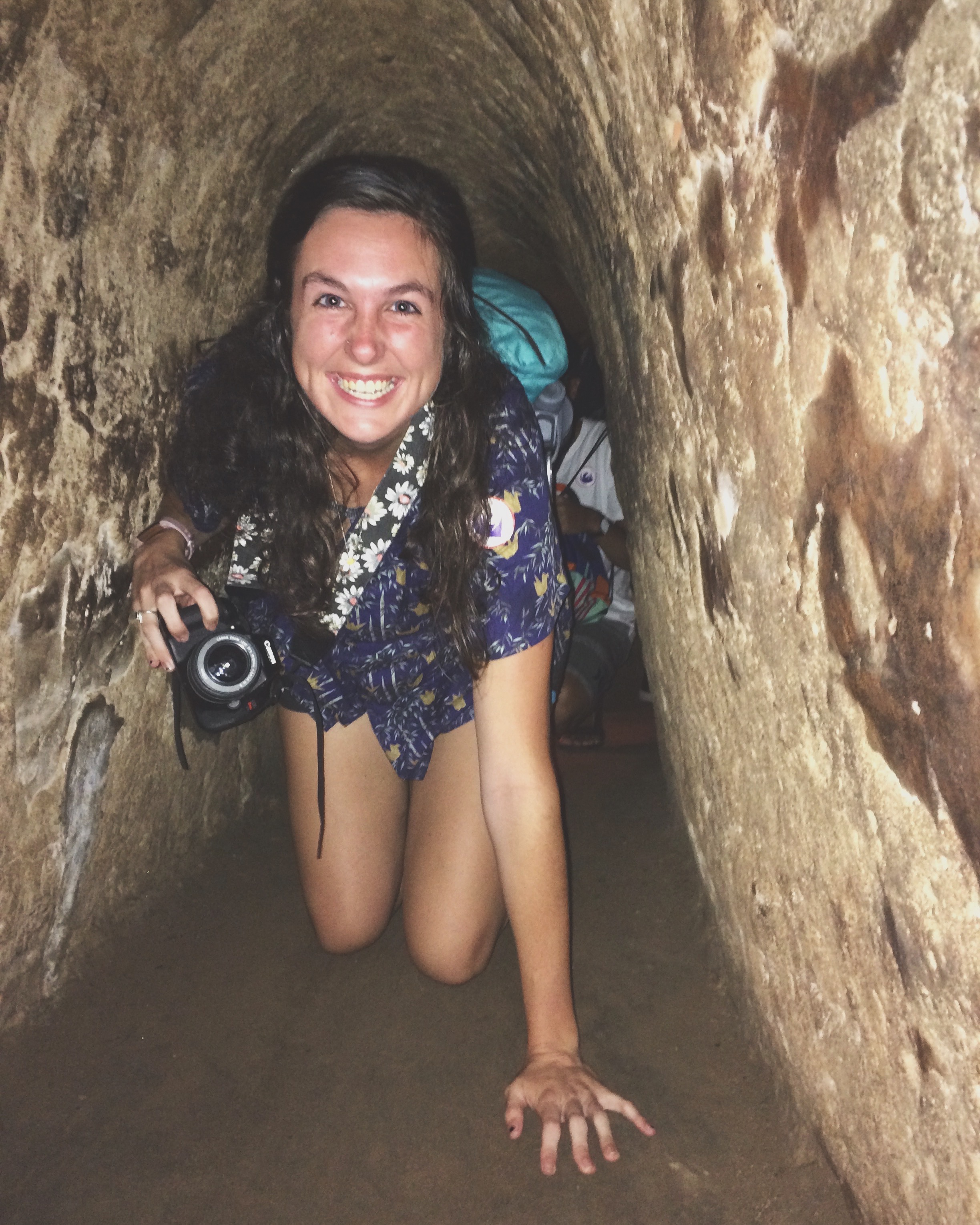 Travel advisor Rachel holding a camera and crawling through a narrow stone tunnel