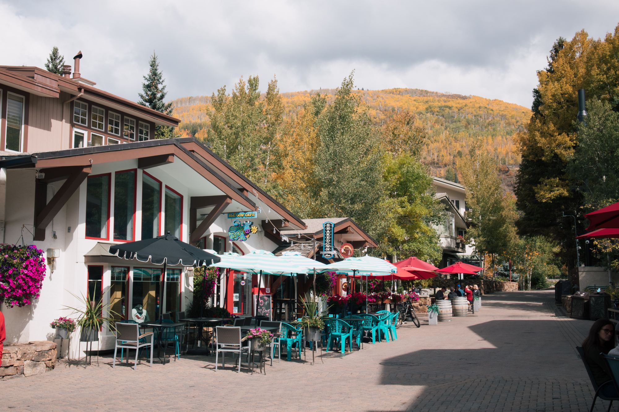 A view of a street with outdoor restaurants with umbrellas at the base of a hill