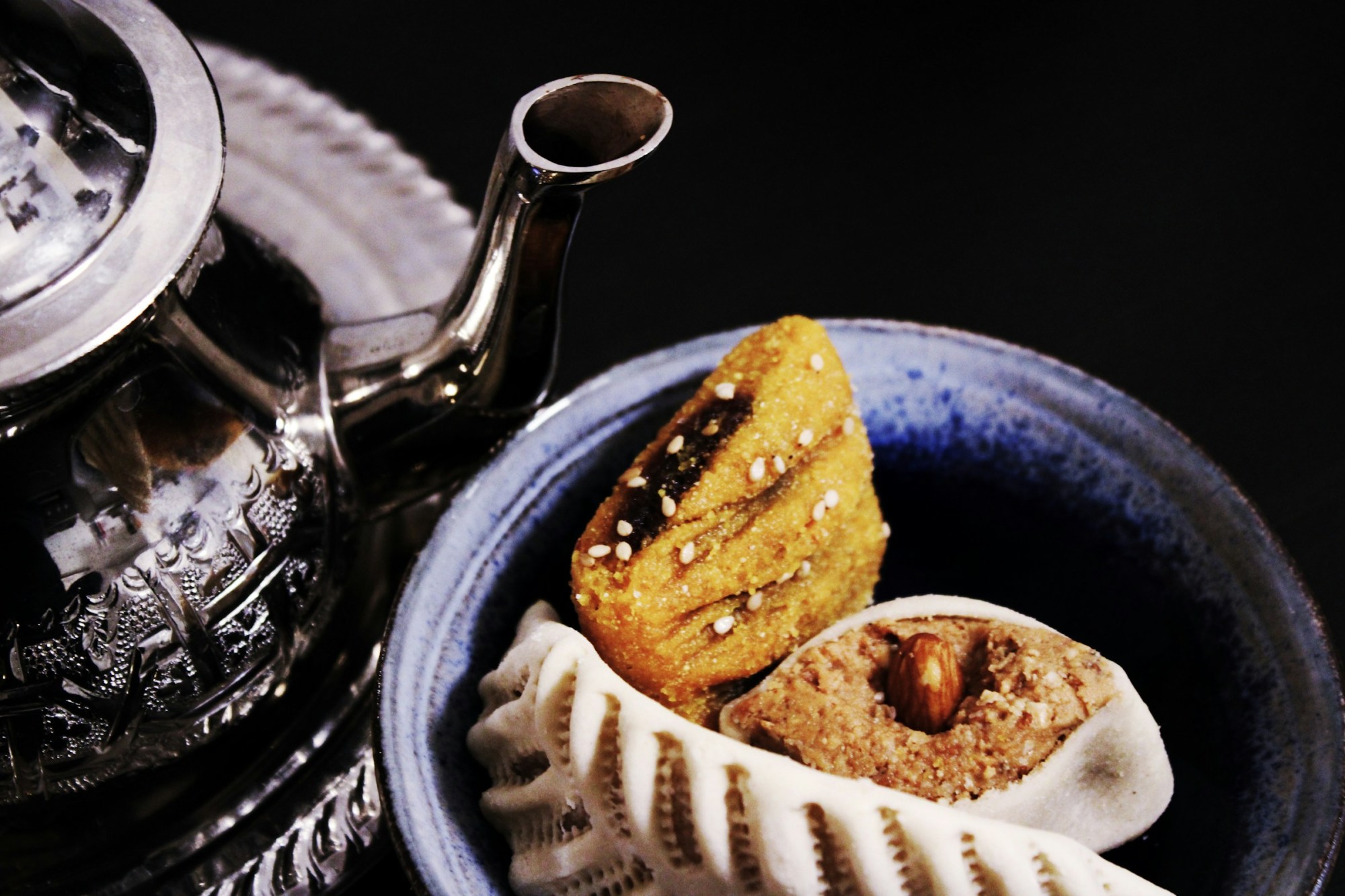A metal tea kettle stands above a traditional clay bowl with homemade pastries