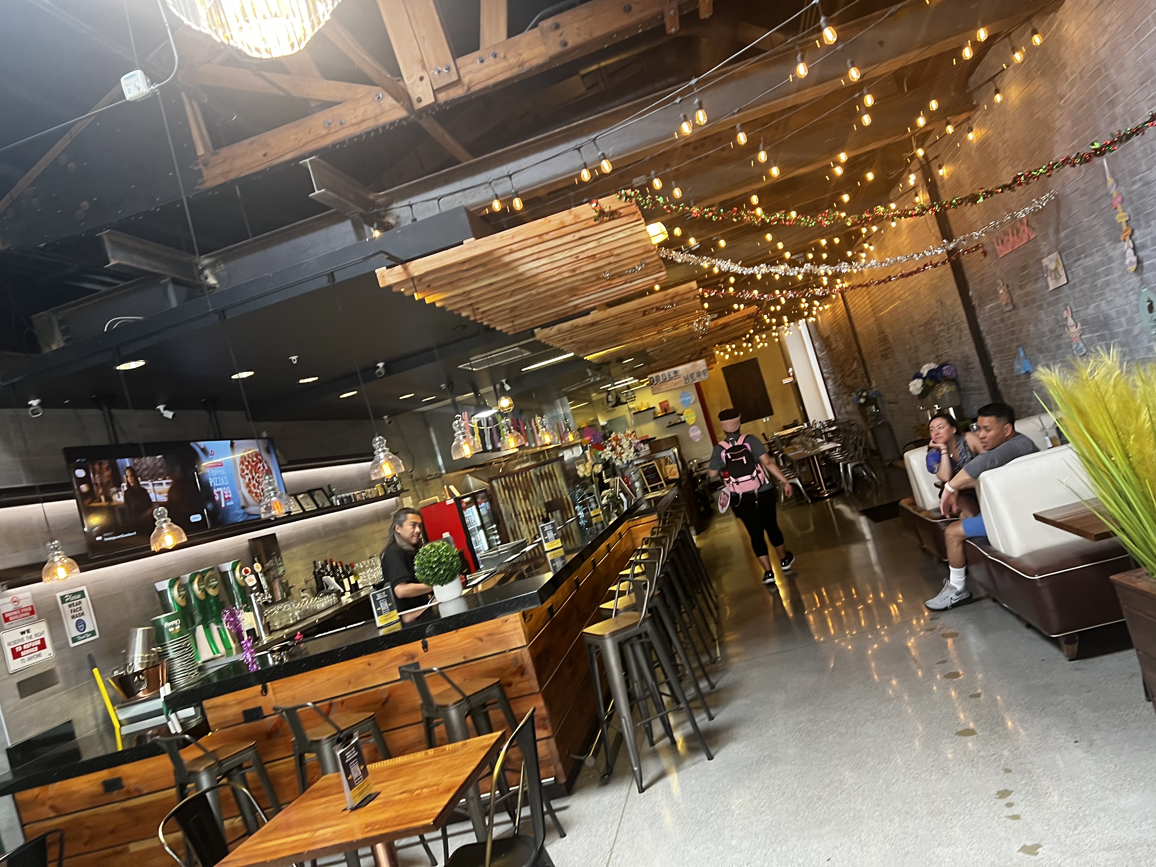 A picture of people having breakfast inside of a restaurant with wooden tables, a bar and string lights.