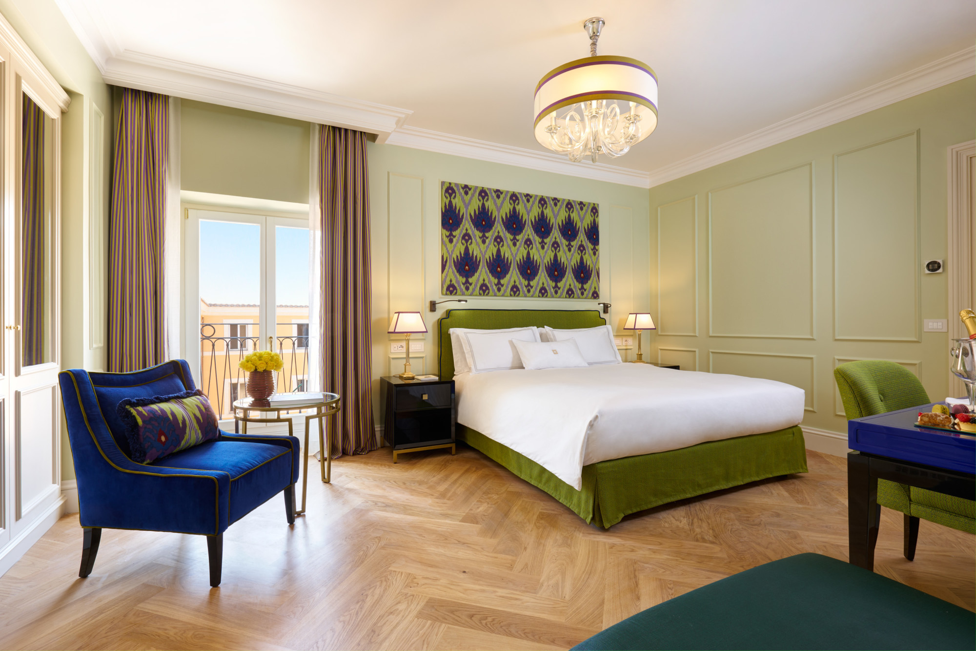 a white bed with green trimming and a blue sofa in a room with wooden floors and pale-green walls