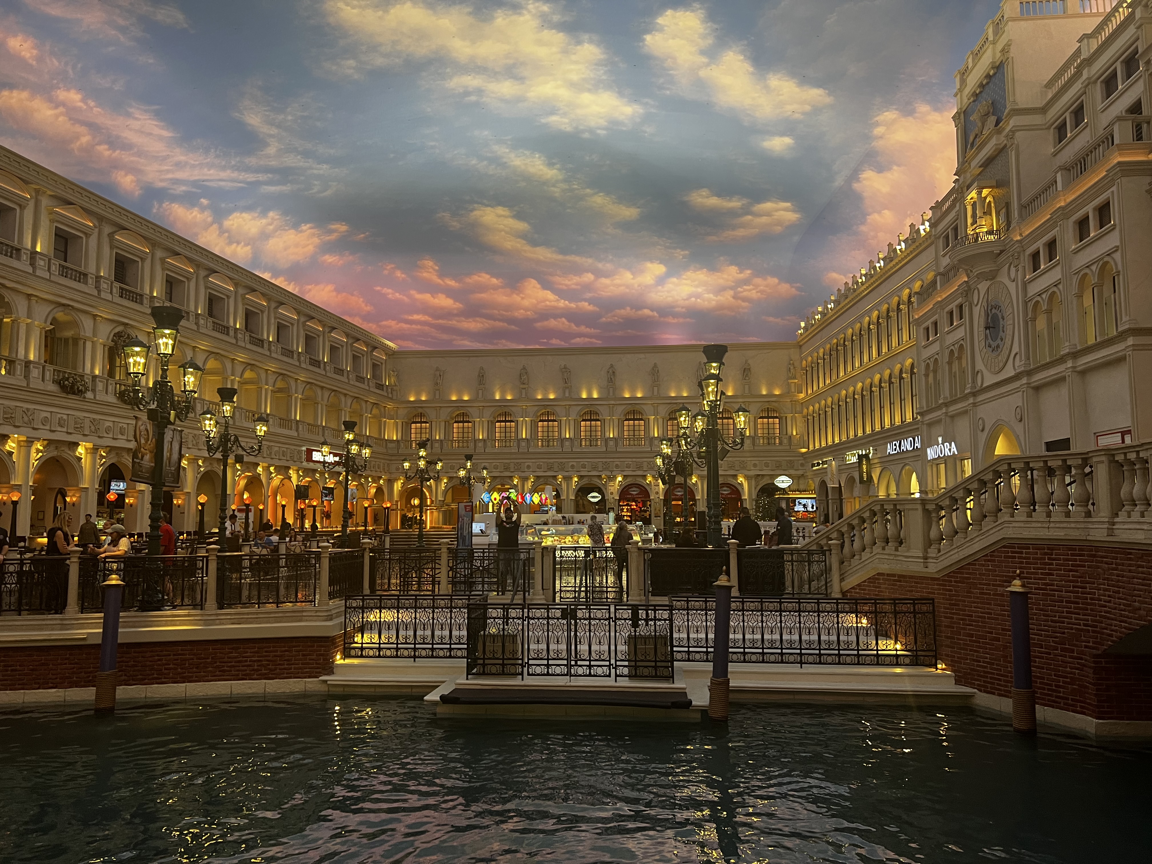 European-style buildings line both sides of the canal, ornate street lamps illuminate the walkways and people enjoy the ambiance.