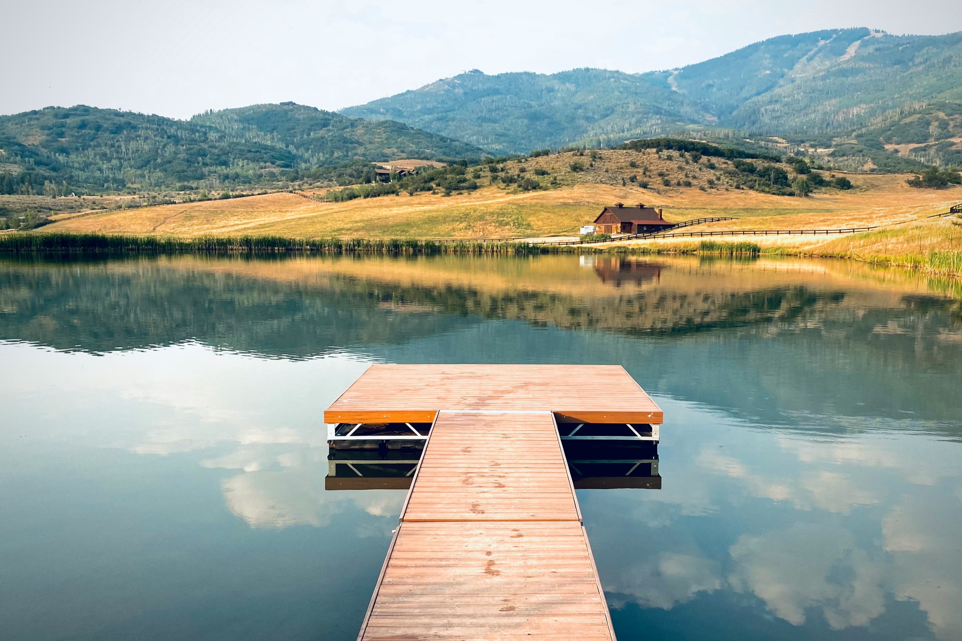 A picture of a dock near a lake and yellow-colored grass during the daytime.