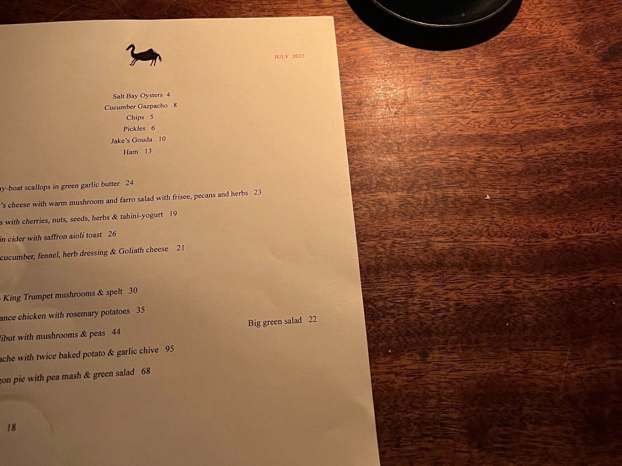 A view of a paper menu with writing on it on top of a wooden table.