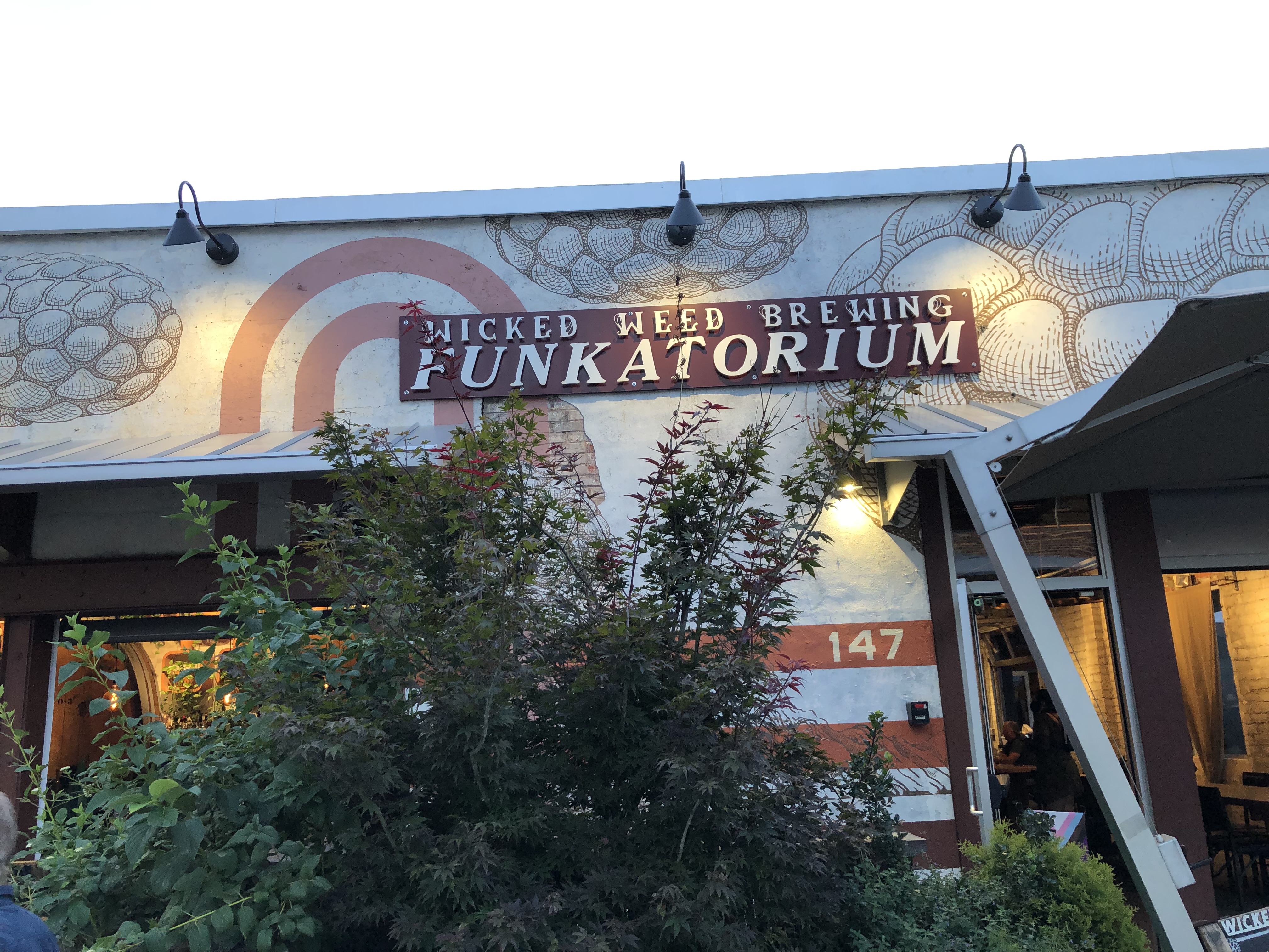 The exterior of Wicked Weed Brewing Funkatorium, a single-story concrete building with a red and white painted sign.