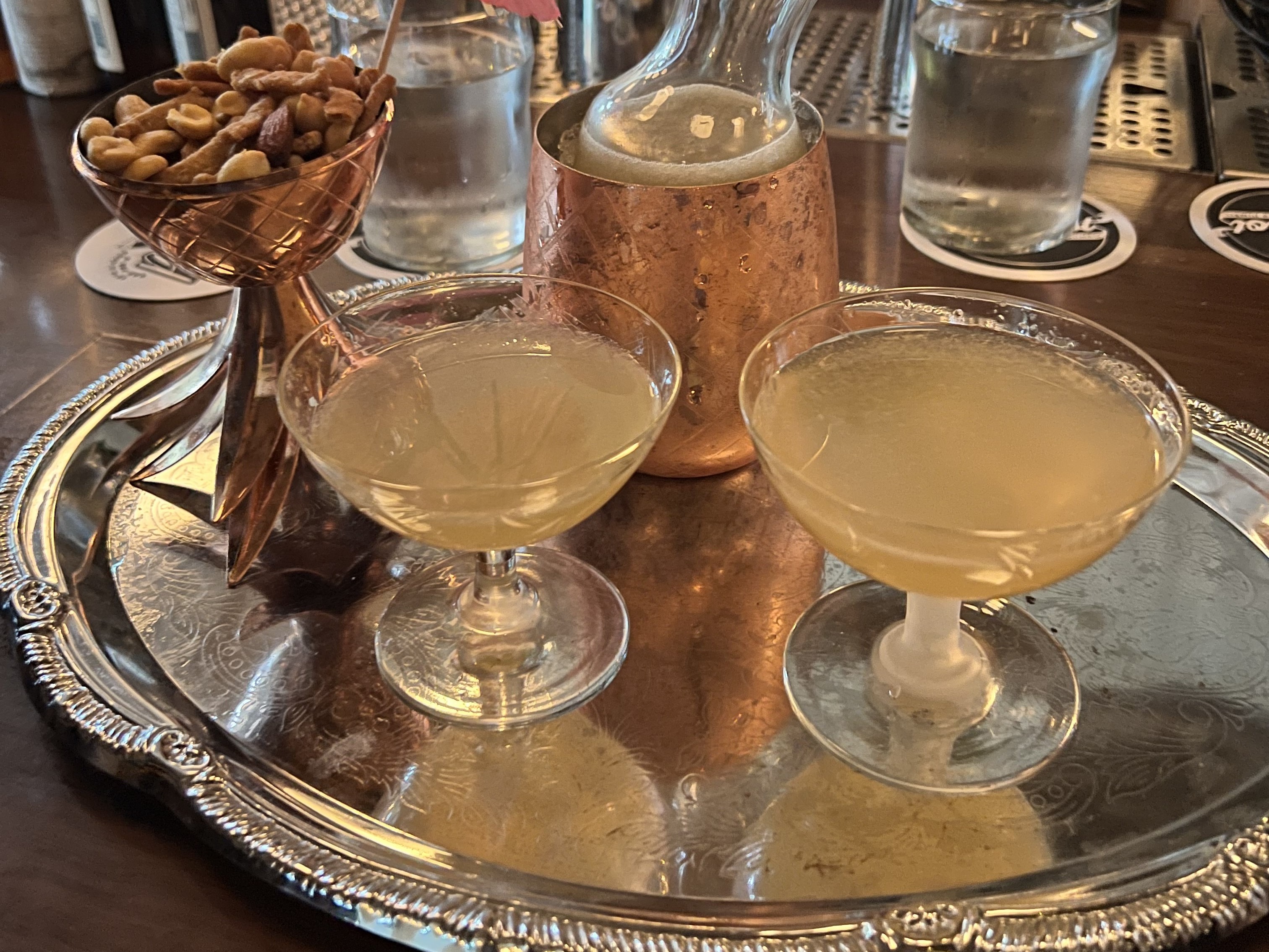 Cocktails on a silver tray on a wooden table.