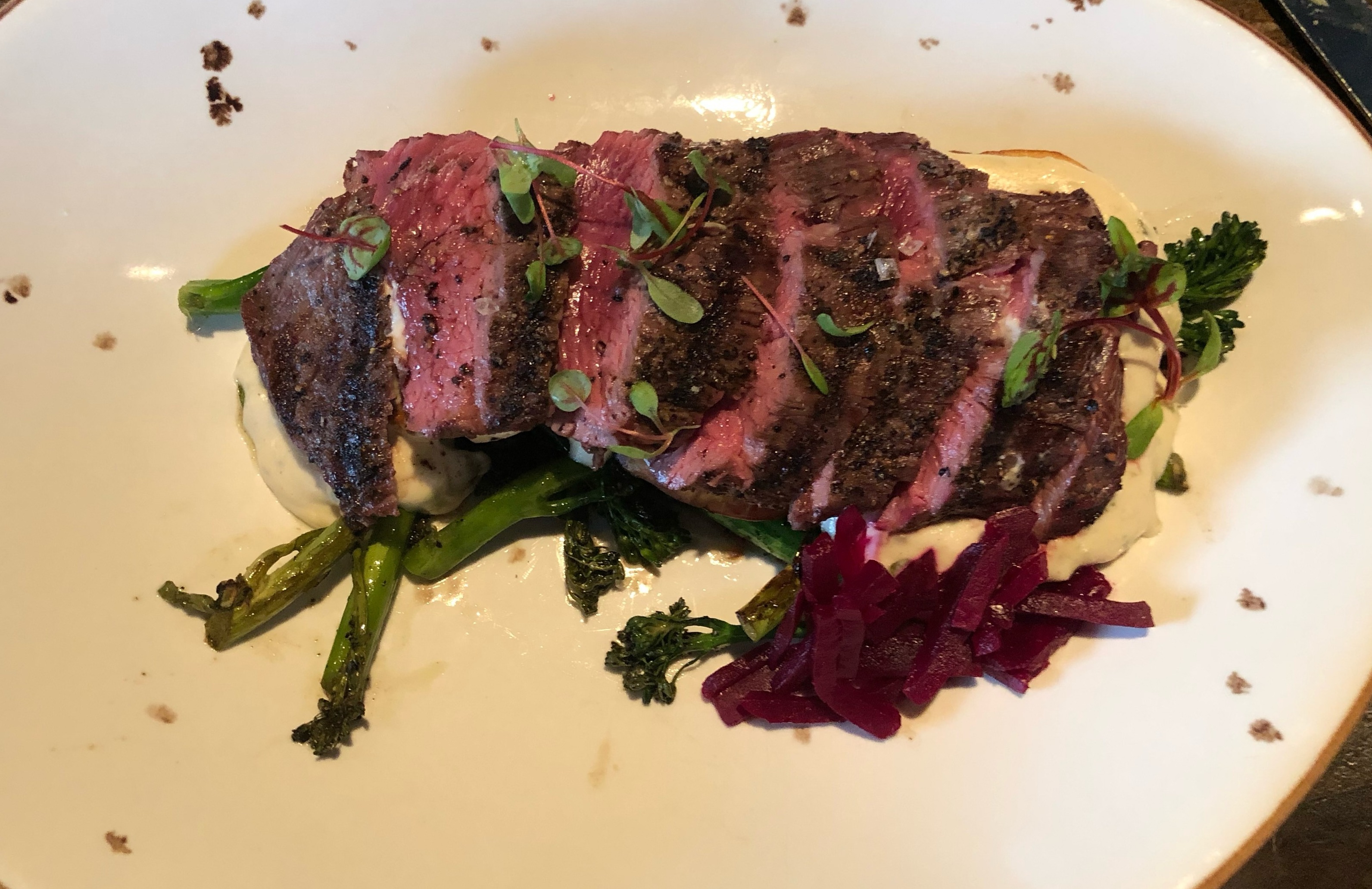 A white plate of steak, herbs and vegetables.