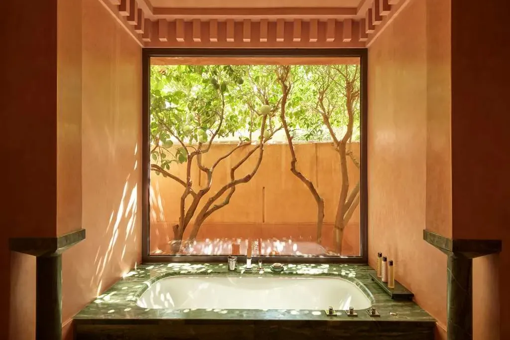 A soak tub surrounded by marble with a view of a private courtyard