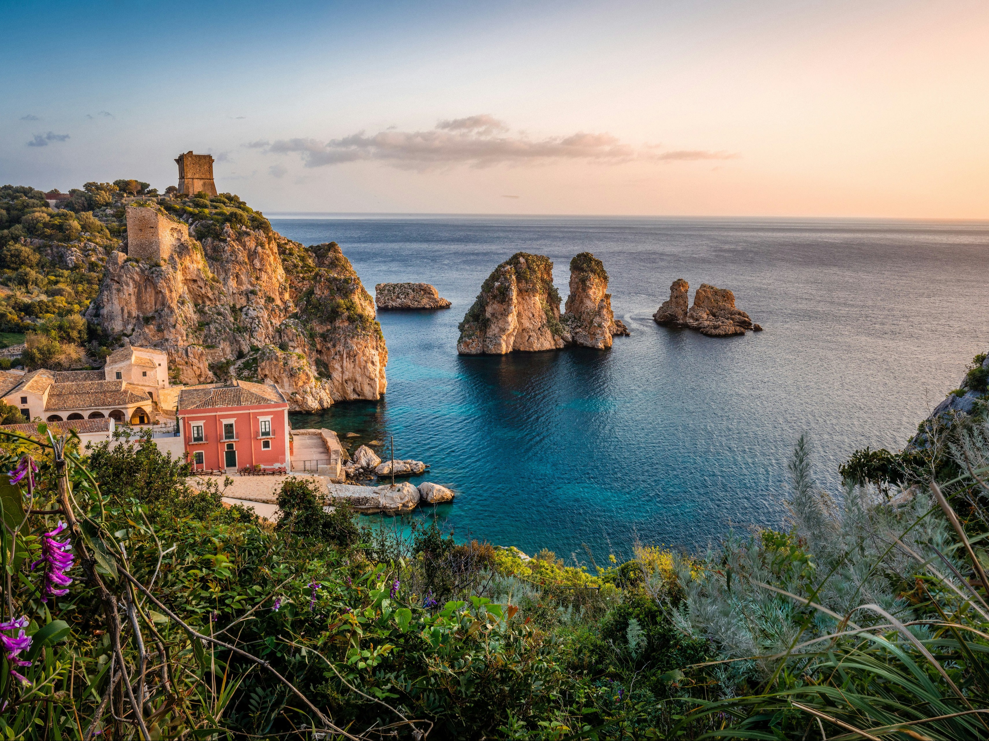 A picture of buildings on the cliff near the sea during sunrise.