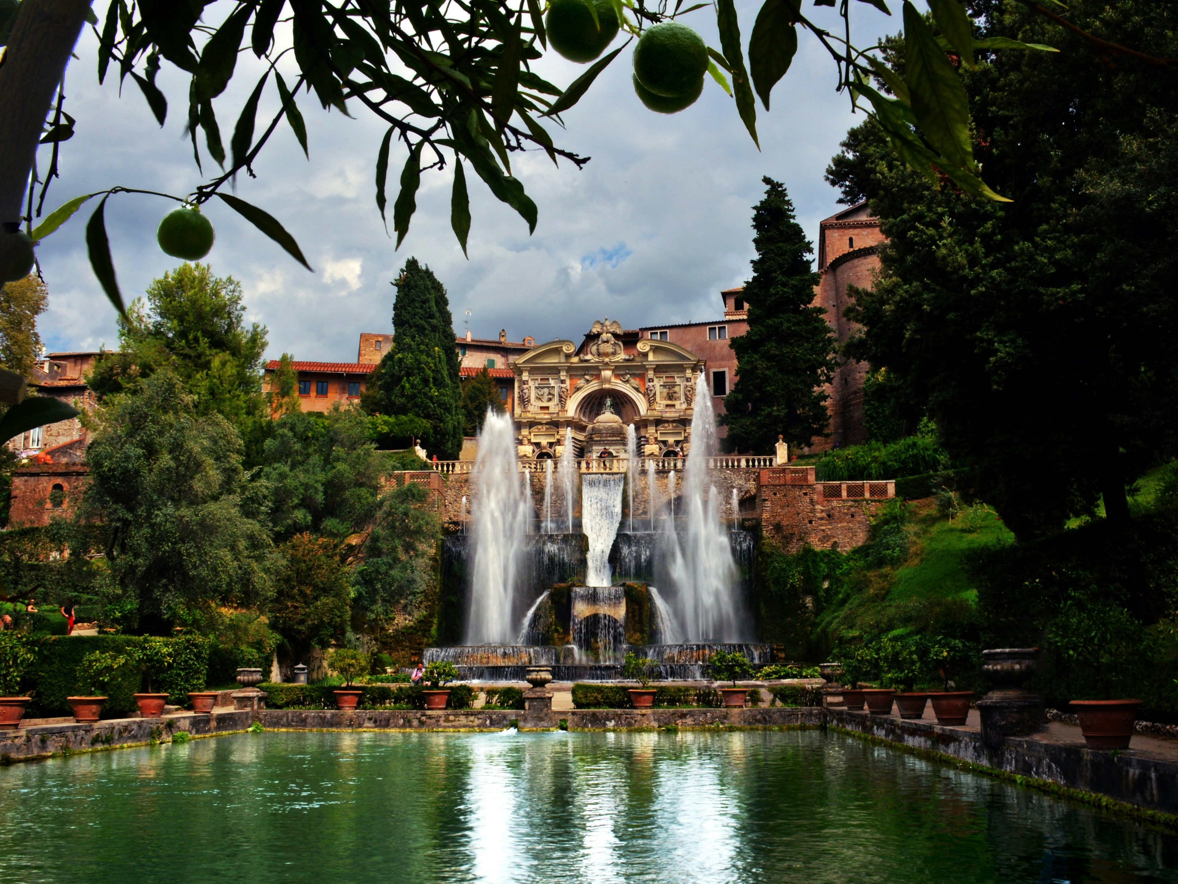 A far view of a fountain surrounded by green trees in the daytime.