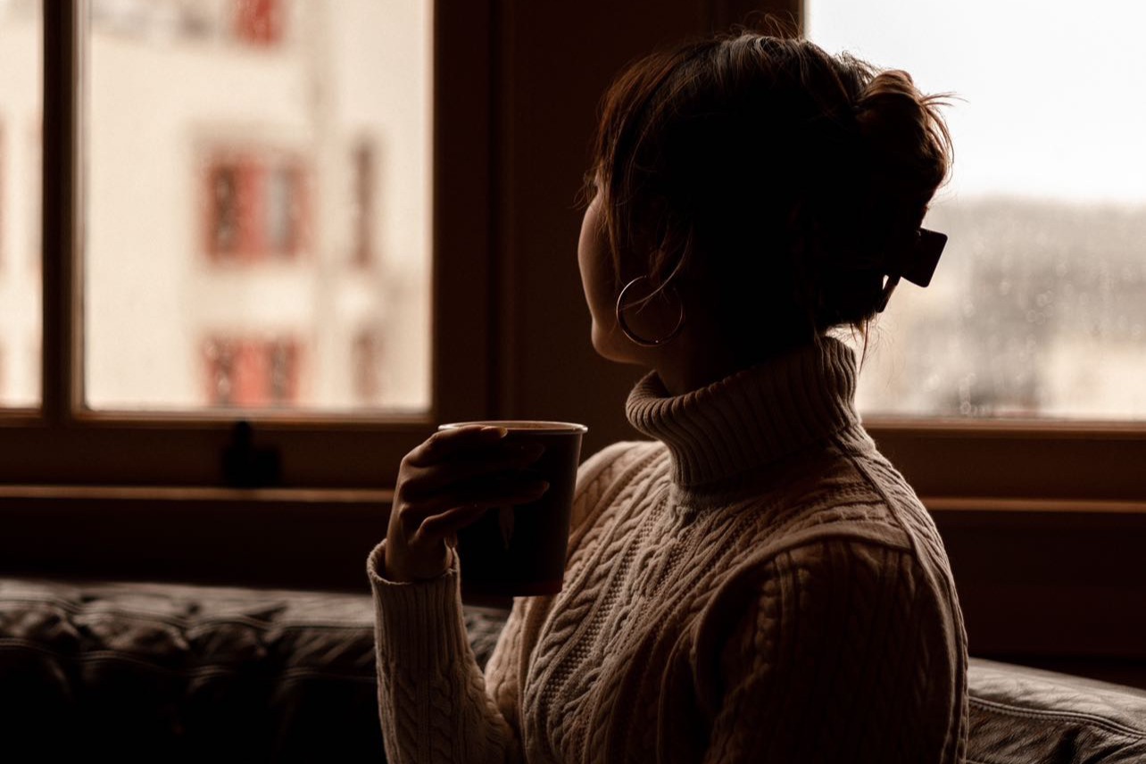A woman holding up a cup of coffee and looking out a window